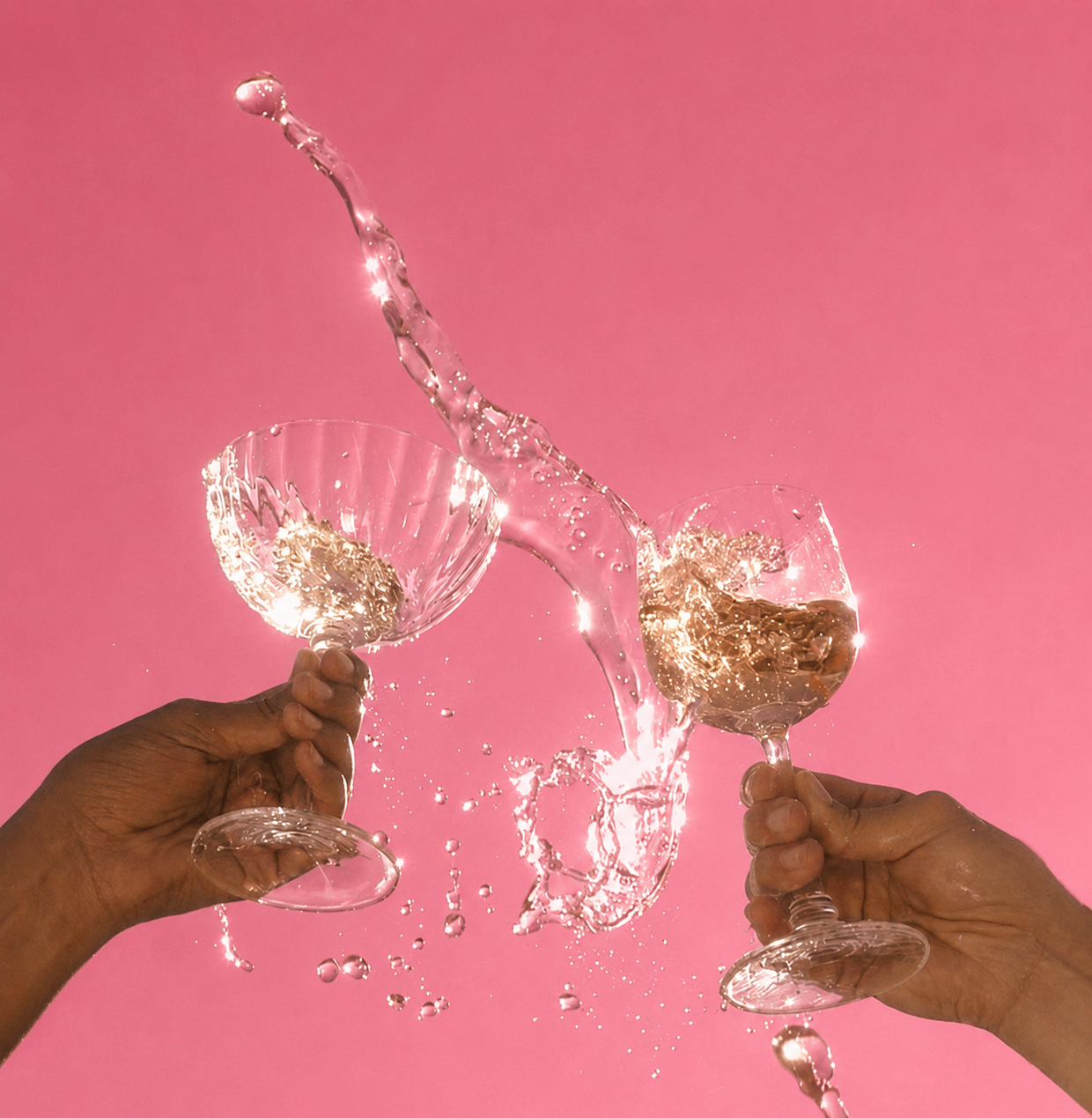 Two people clinking wine glasses with liquid splashing in the air, set against a clear blue sky.