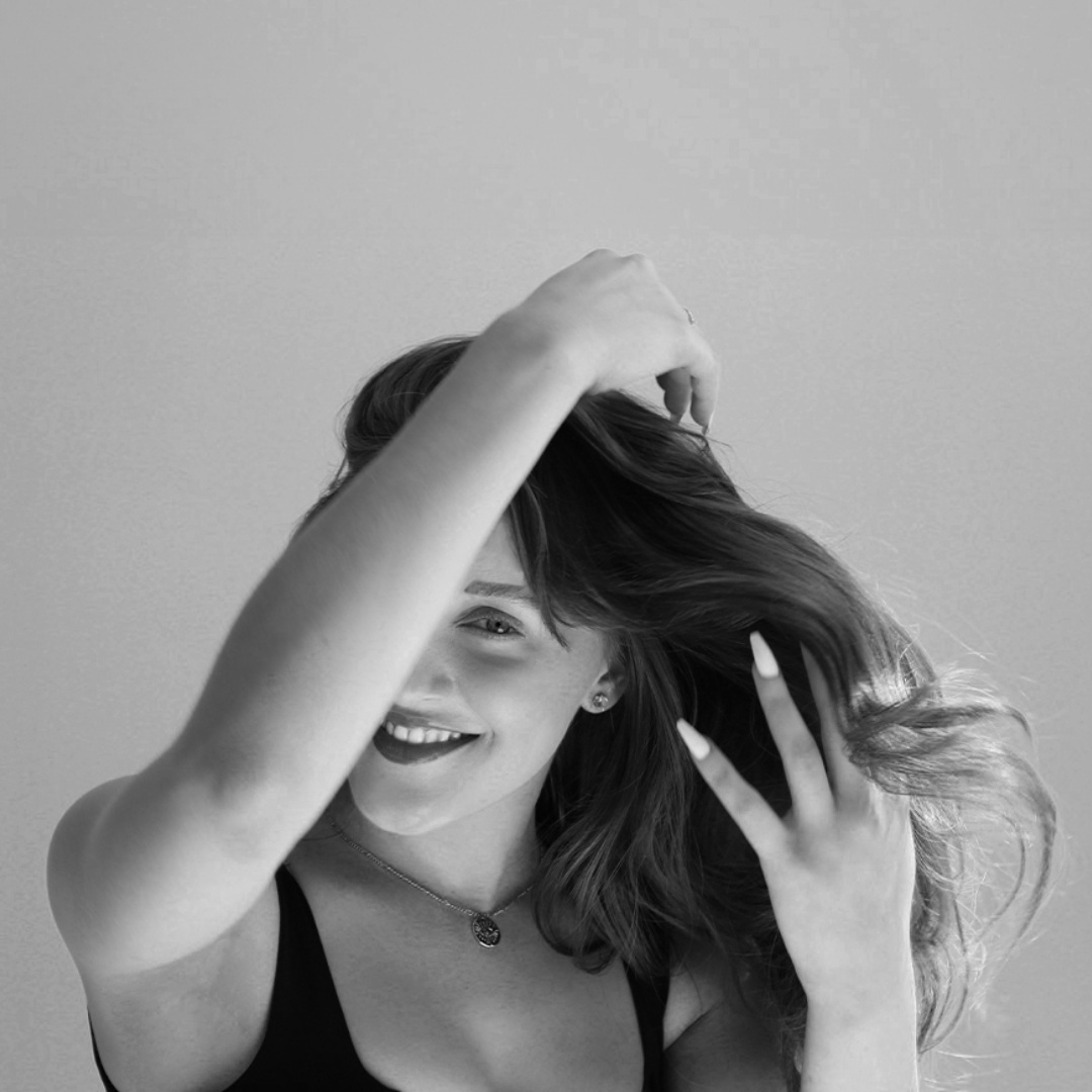 Black and white photo of a woman smiling while touching her hair.