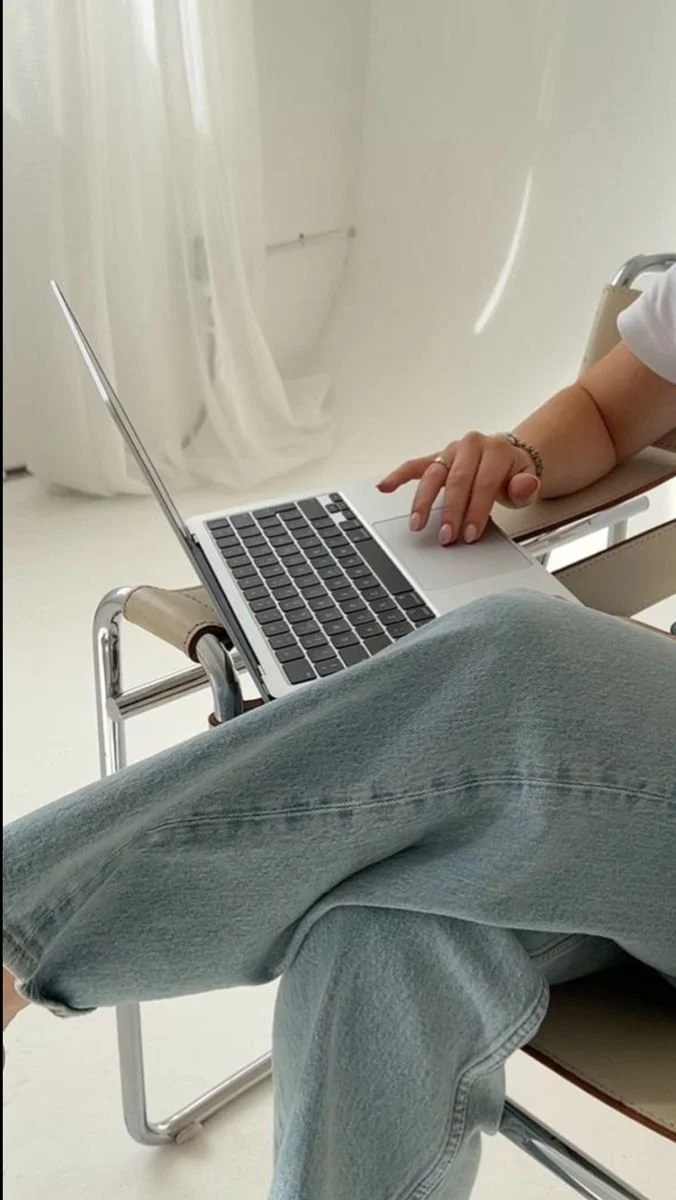 Person using a laptop on their lap while sitting in a chair, with crossed legs in jeans.