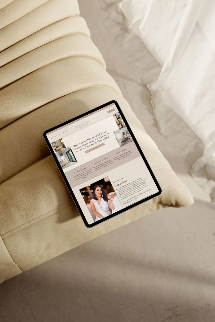 Tablet displaying an interior design website, placed on a beige cushioned surface, with white curtains in the background.