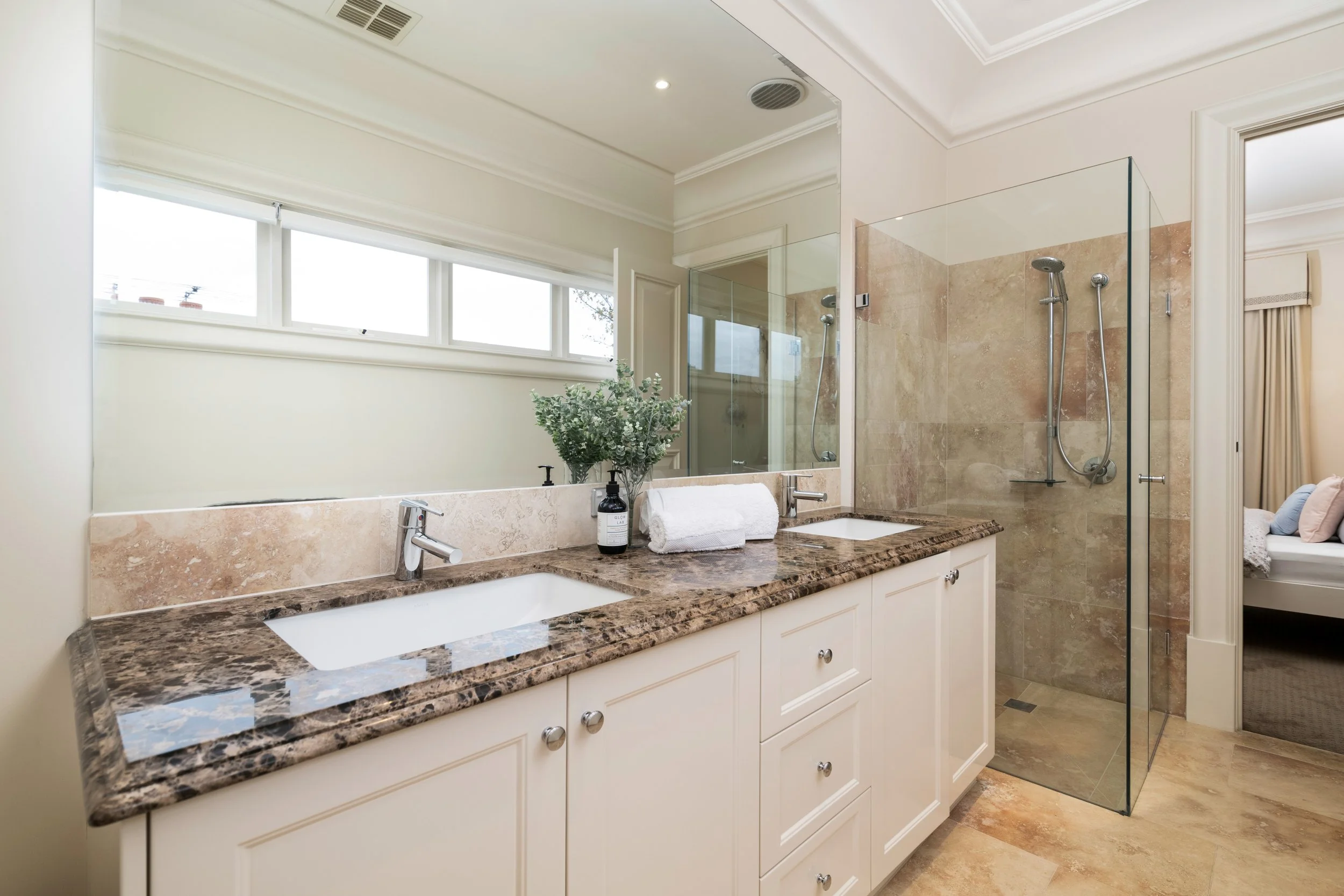 Bathroom with dual sinks, marble countertops, large mirror, and walk-in shower with glass enclosure.