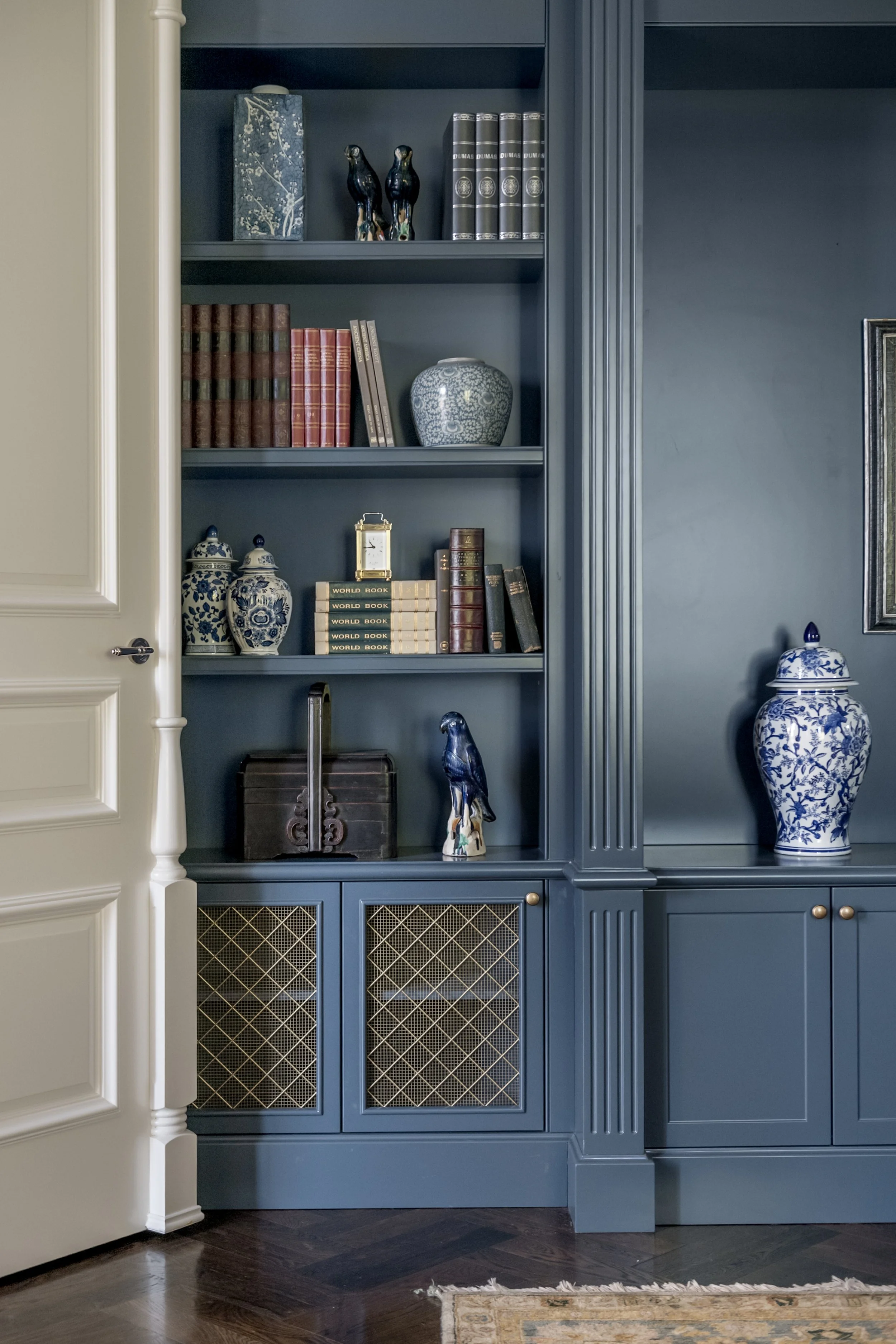Blue built-in bookshelf with decorative porcelain vases, antique books, and small statuettes inside a room.