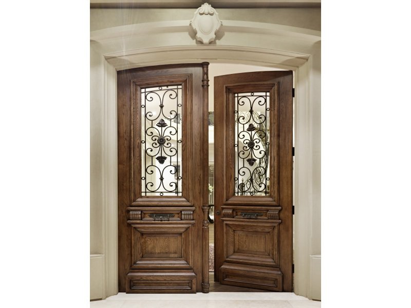 Double wooden doors with ornate wrought iron designs and glass panels, set in a classical entryway with decorative molding.