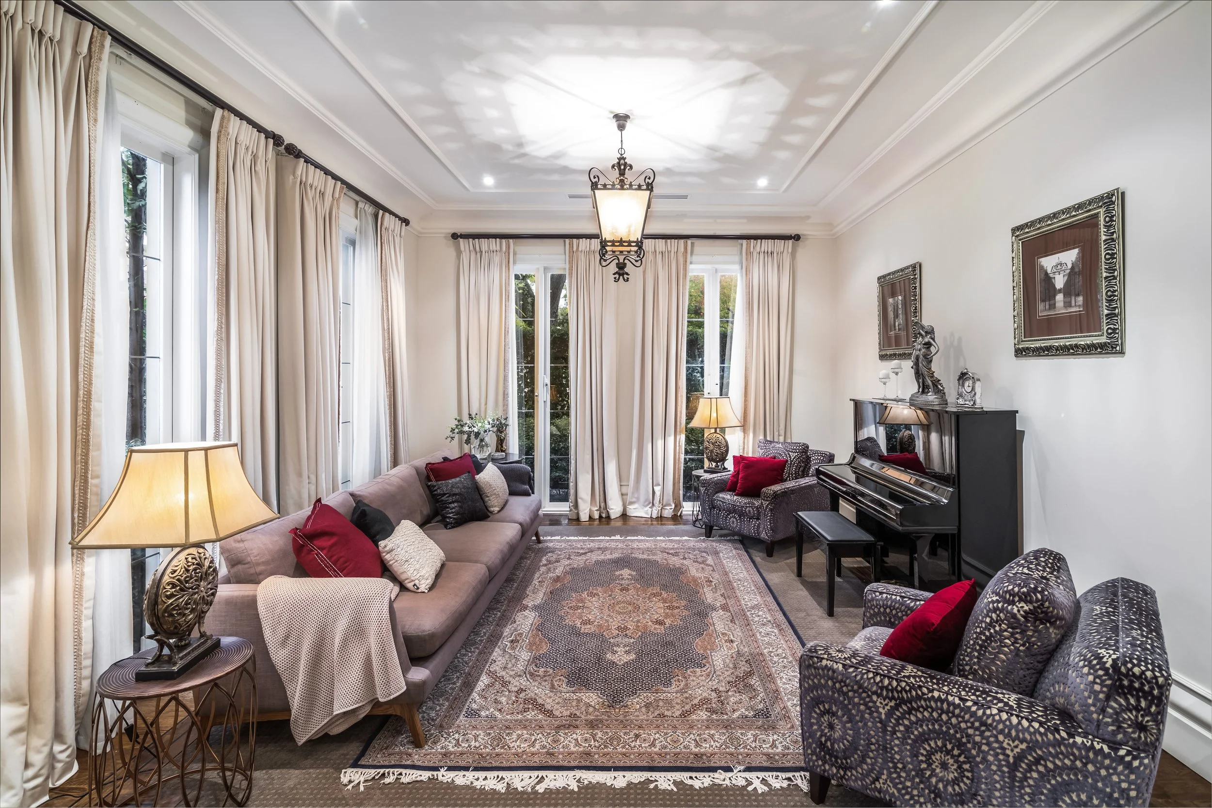 Decorative living room with beige sofa, armchairs, area rug, piano, side tables, lamps, framed art, and large windows with curtains.
