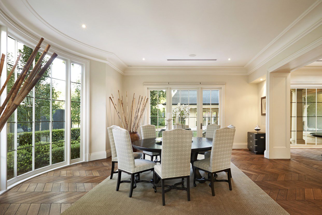 Bright dining room with a round table, six upholstered chairs, large windows, and sliding glass doors leading to a backyard.