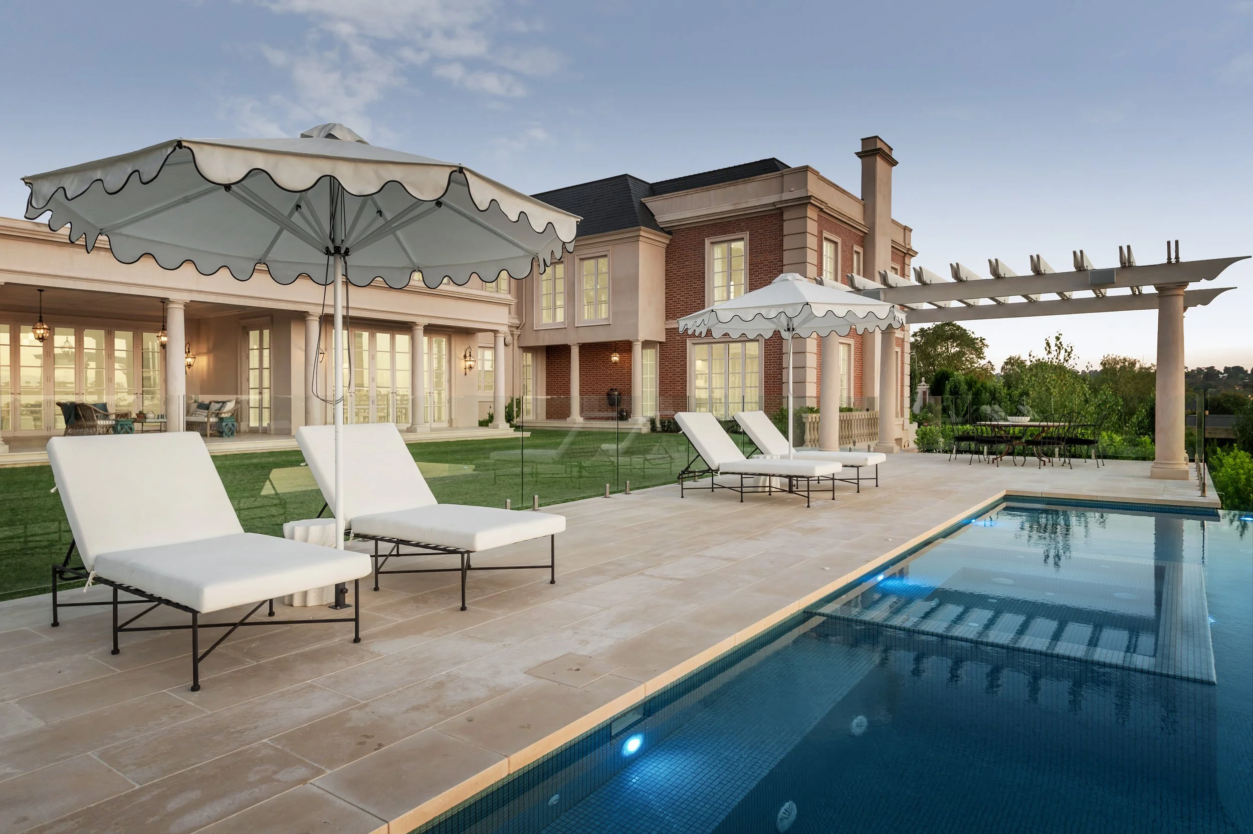 Luxury backyard with swimming pool, lounge chairs, umbrellas, and elegant house in the background.