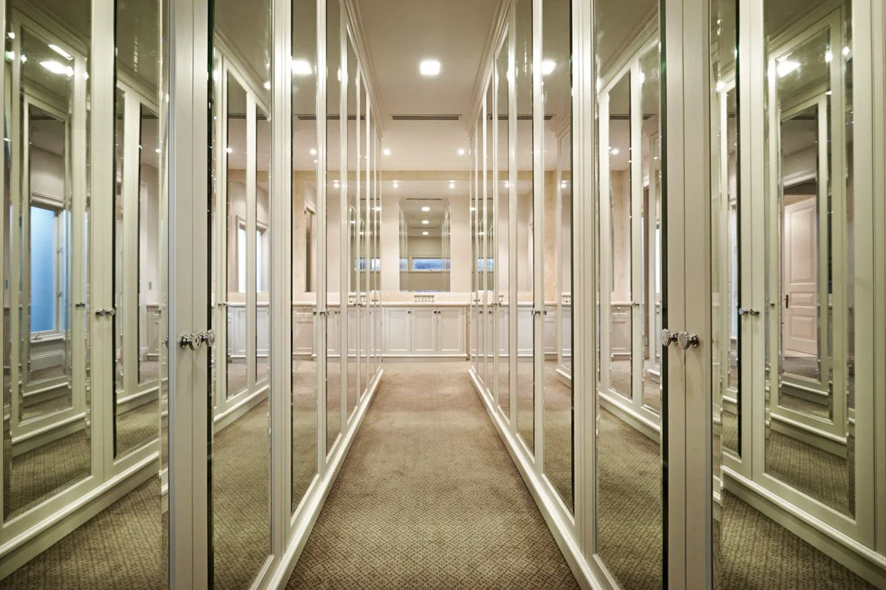A boutique fitting room with multiple mirrored doors on both sides and beige carpeted floor.