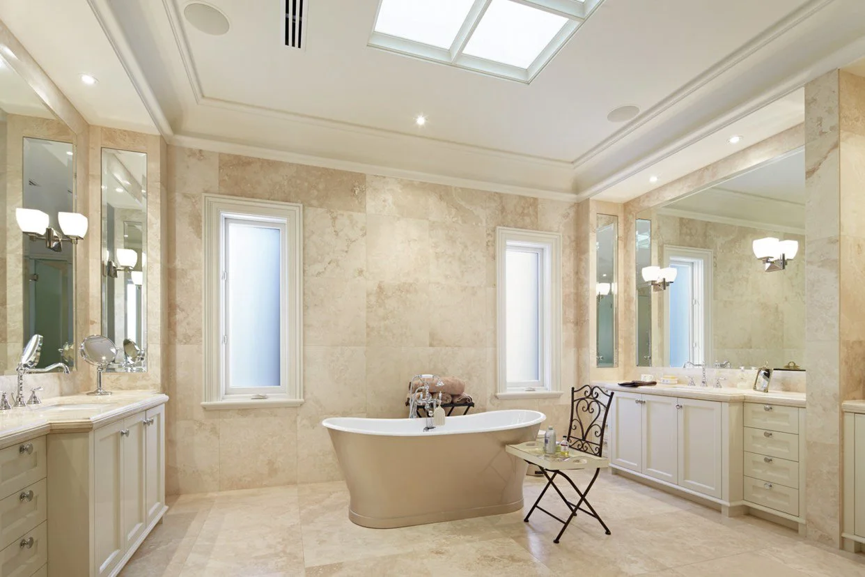 Luxurious bathroom with a free-standing bathtub, multiple mirrors, and vanity cabinets. Natural light from skylights and windows brightens the space.
