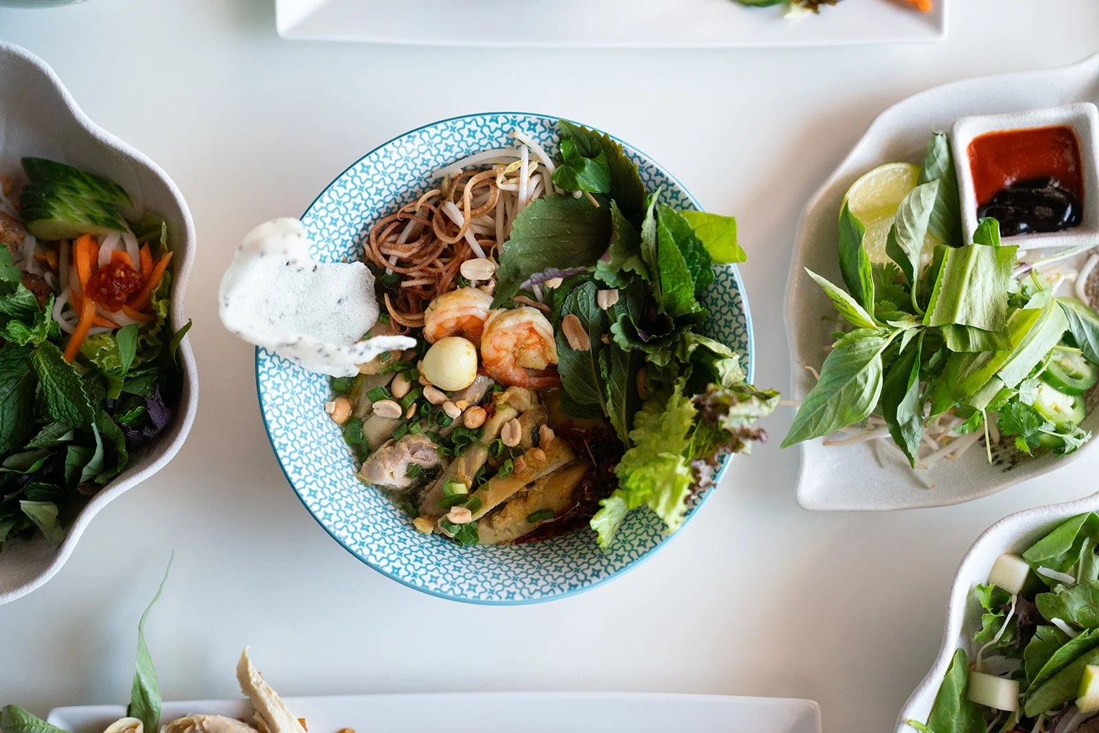 Our M&igrave; Quảng features turmeric-infused noodles tossed in a light, gravy-style broth &mdash; just enough to coat, never overwhelm.
Tender chicken, shrimp, fresh herbs, and roasted peanuts bring brightness and texture to every bite.
A traditiona