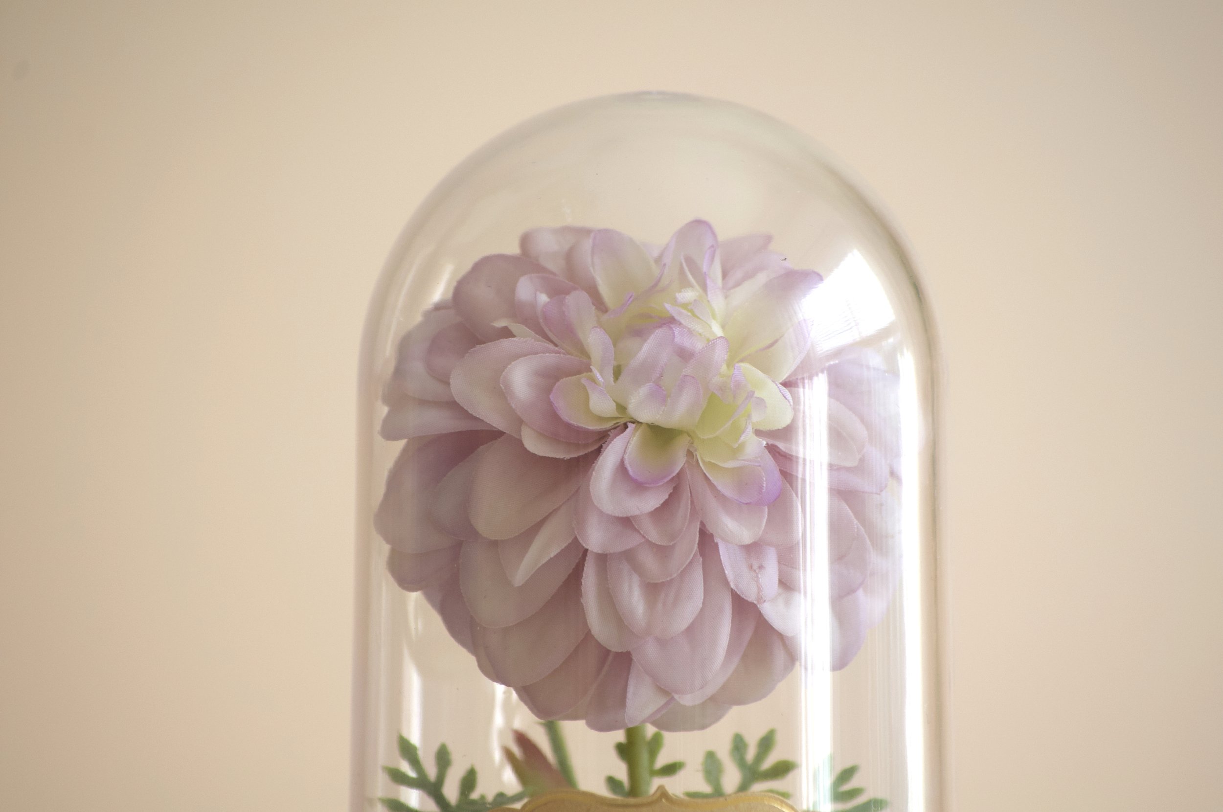 Artificial pink flower inside a glass dome on a beige background.