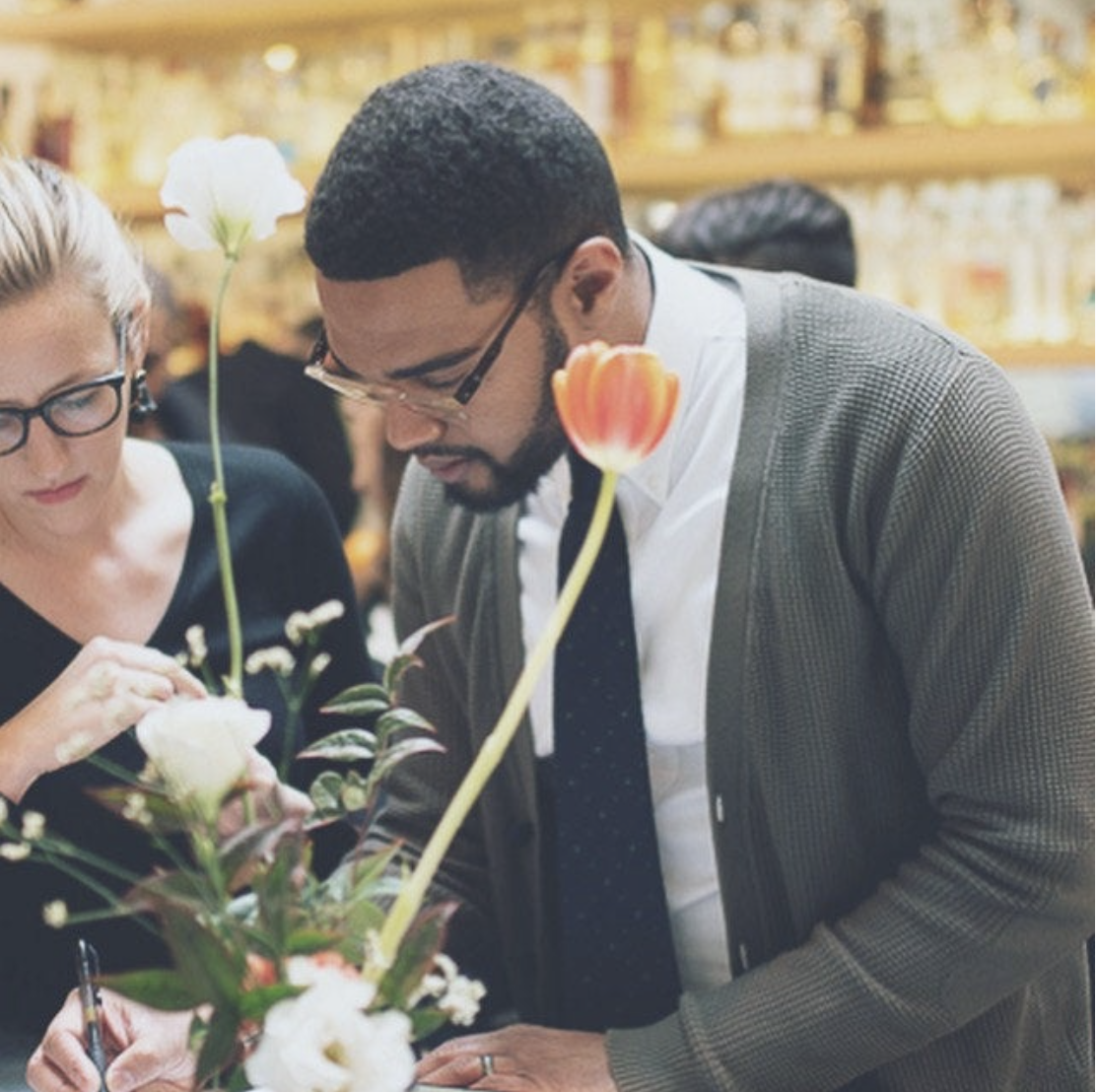 Two people examining a flower arrangement in a bar or restaurant setting.