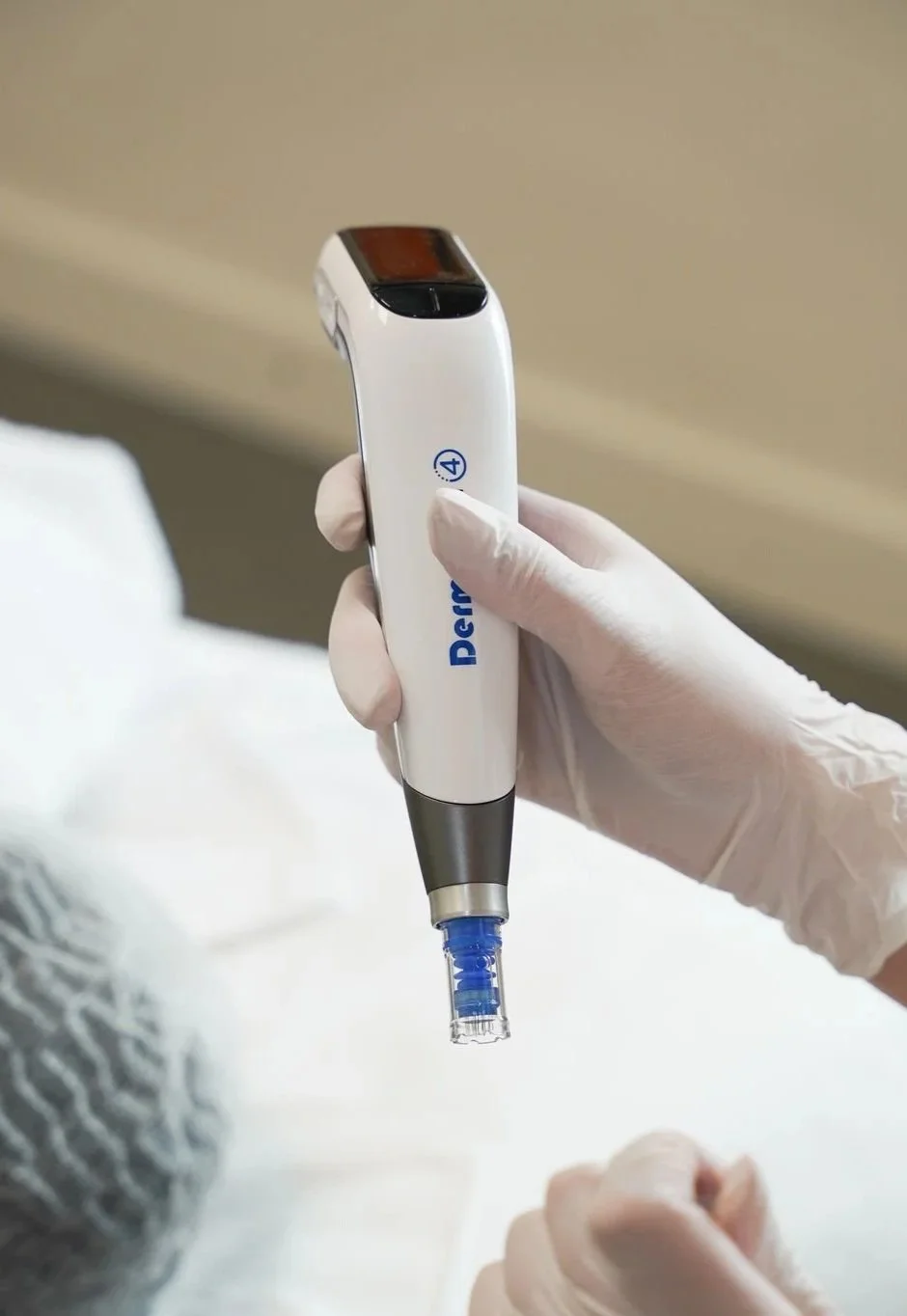 A healthcare worker wearing gloves holding a DermLite dermatoscope device, used for skin examination, over a patient's hand.