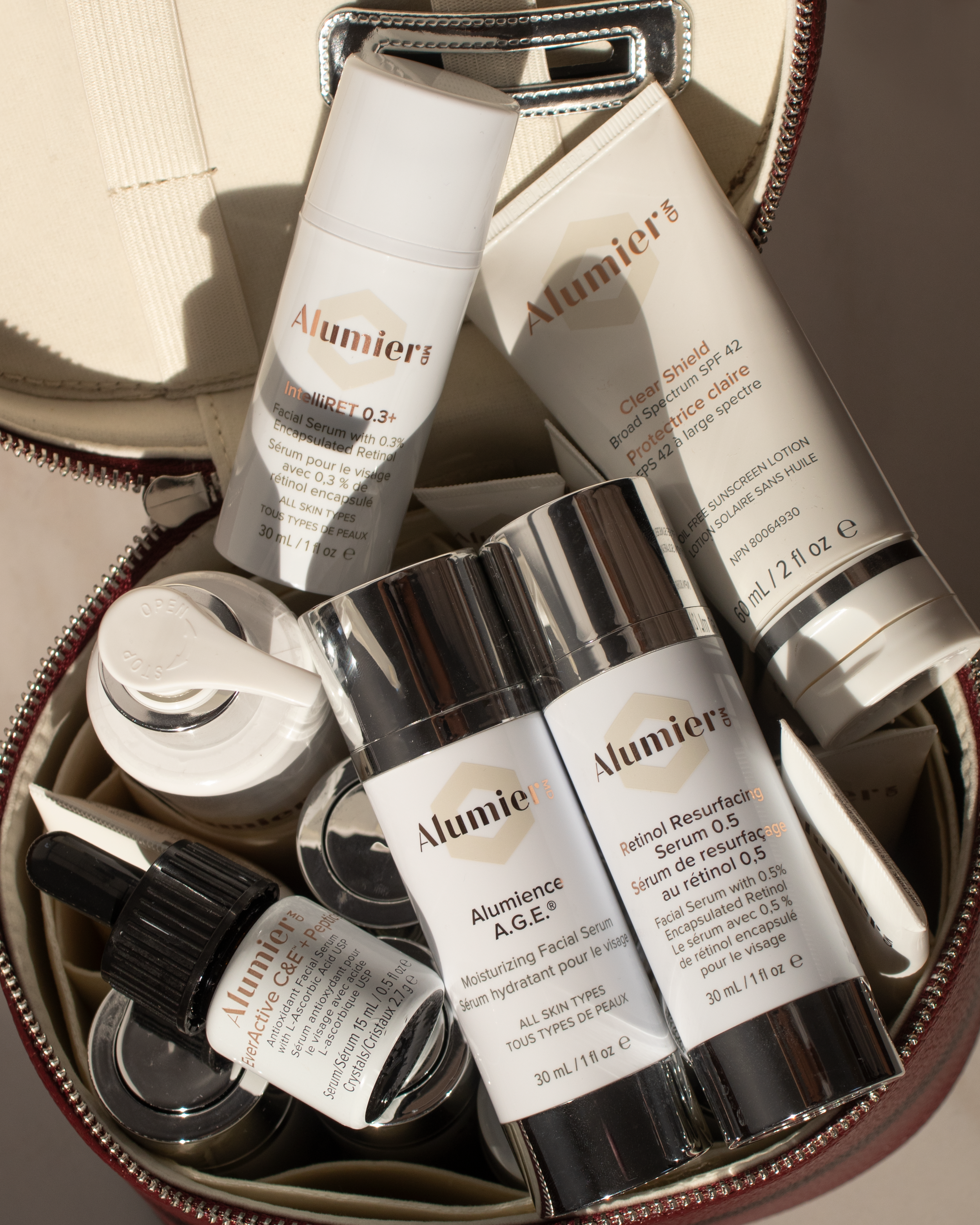 Collection of skincare and sunscreen products in a round makeup bag, including facial serums, moisturizers, and broad-spectrum sunscreens labeled Alumier.