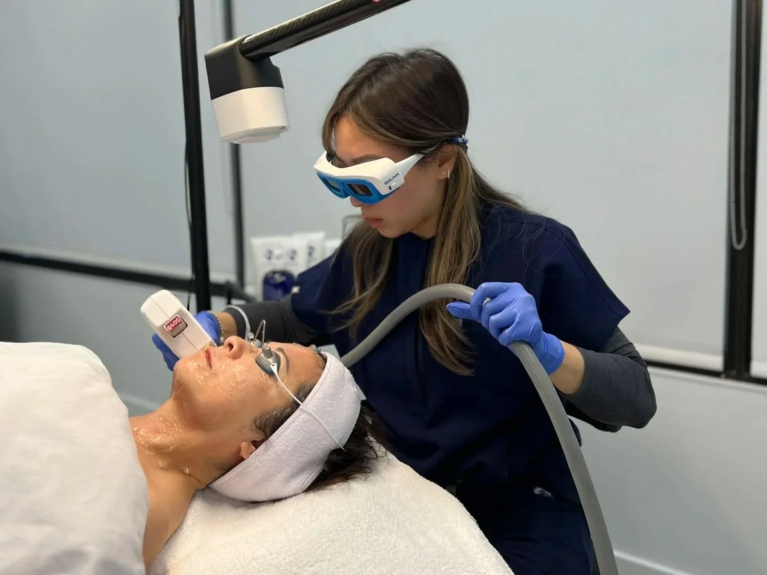 A woman receiving a laser treatment on her face from a healthcare professional in a clinical setting.