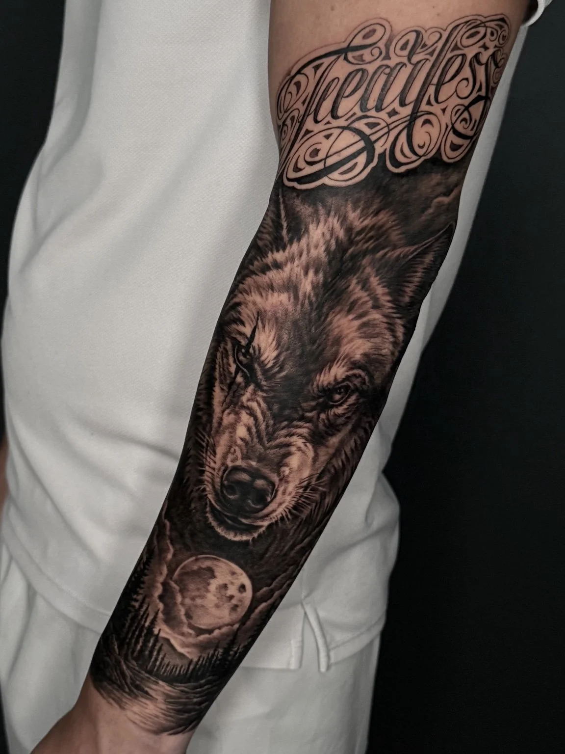 Realistic wolf and moon forearm tattoo with script by Alina Horobets, Bournemouth