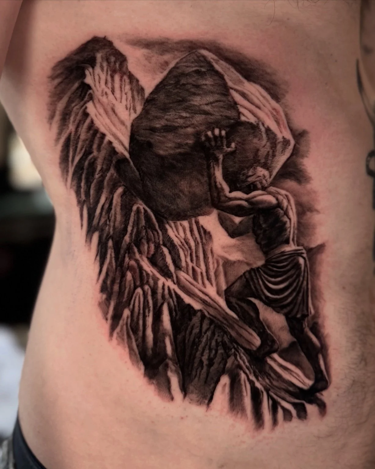 Black and grey tattoo of a figure carrying a rocky globe by Alina Horobets, Bournemouth