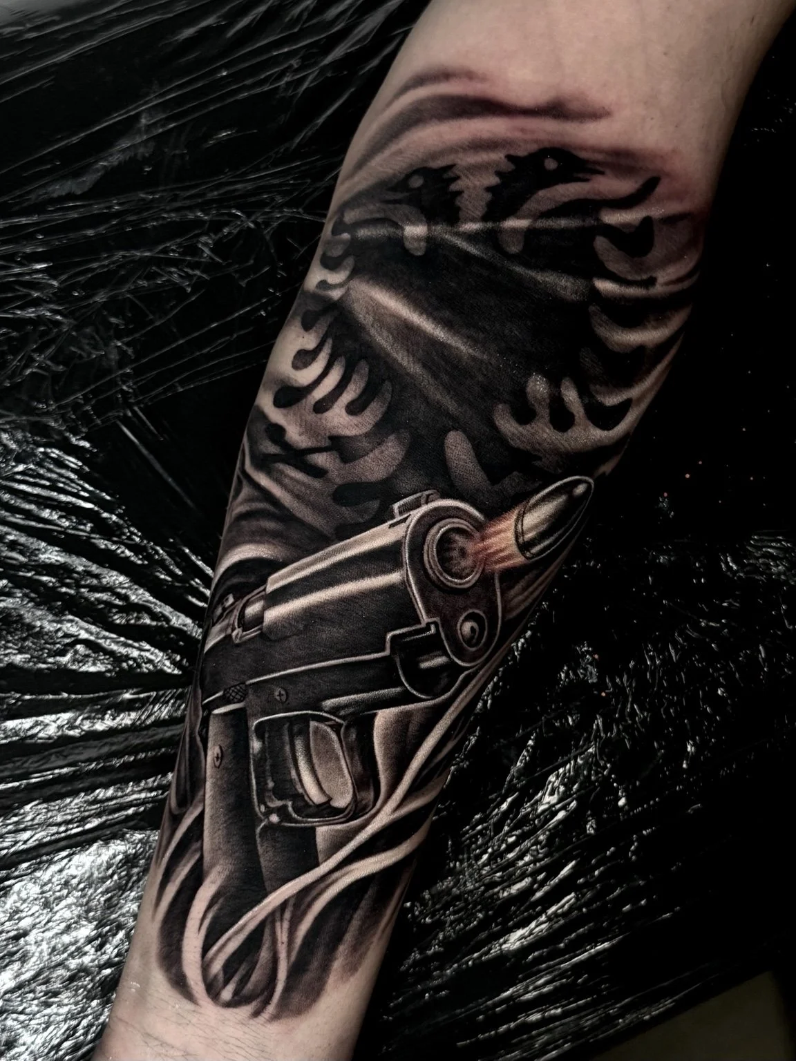 Black and grey eagle and pistol forearm tattoo by Alina Horobets, Bournemouth
