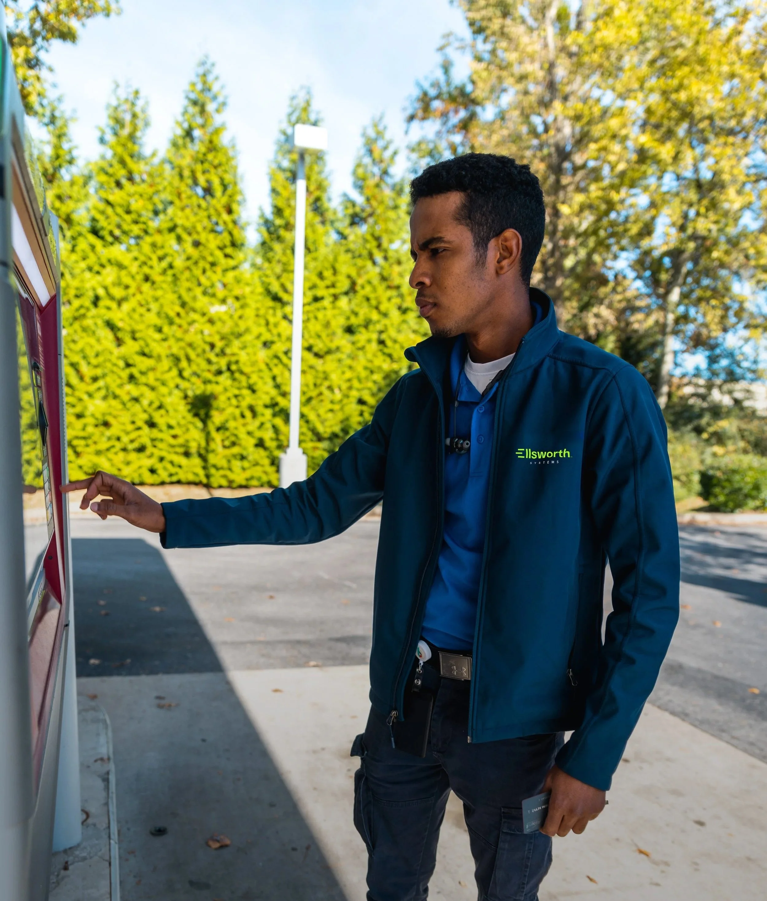 A person in a blue jacket using an ATM outdoors.
