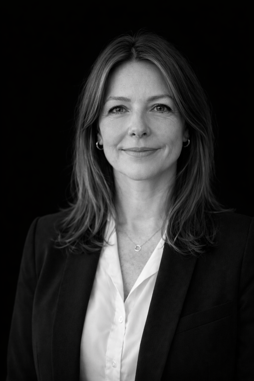 A black and white portrait of a smiling woman with shoulder-length hair, wearing a suit jacket and a white blouse, against a dark background.