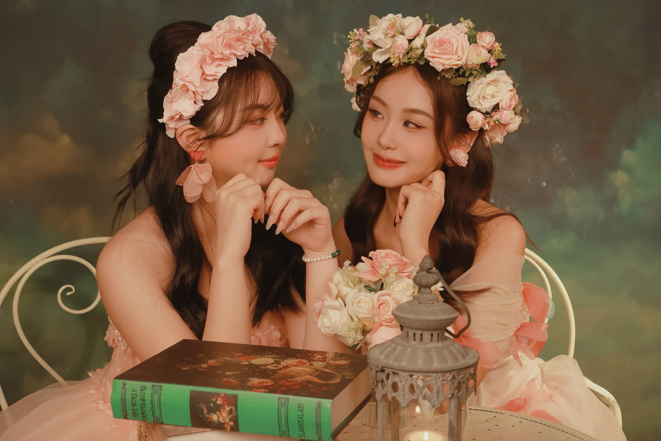Two females in pink rose princess dresses with a tea table against french oil painting studio backdrop