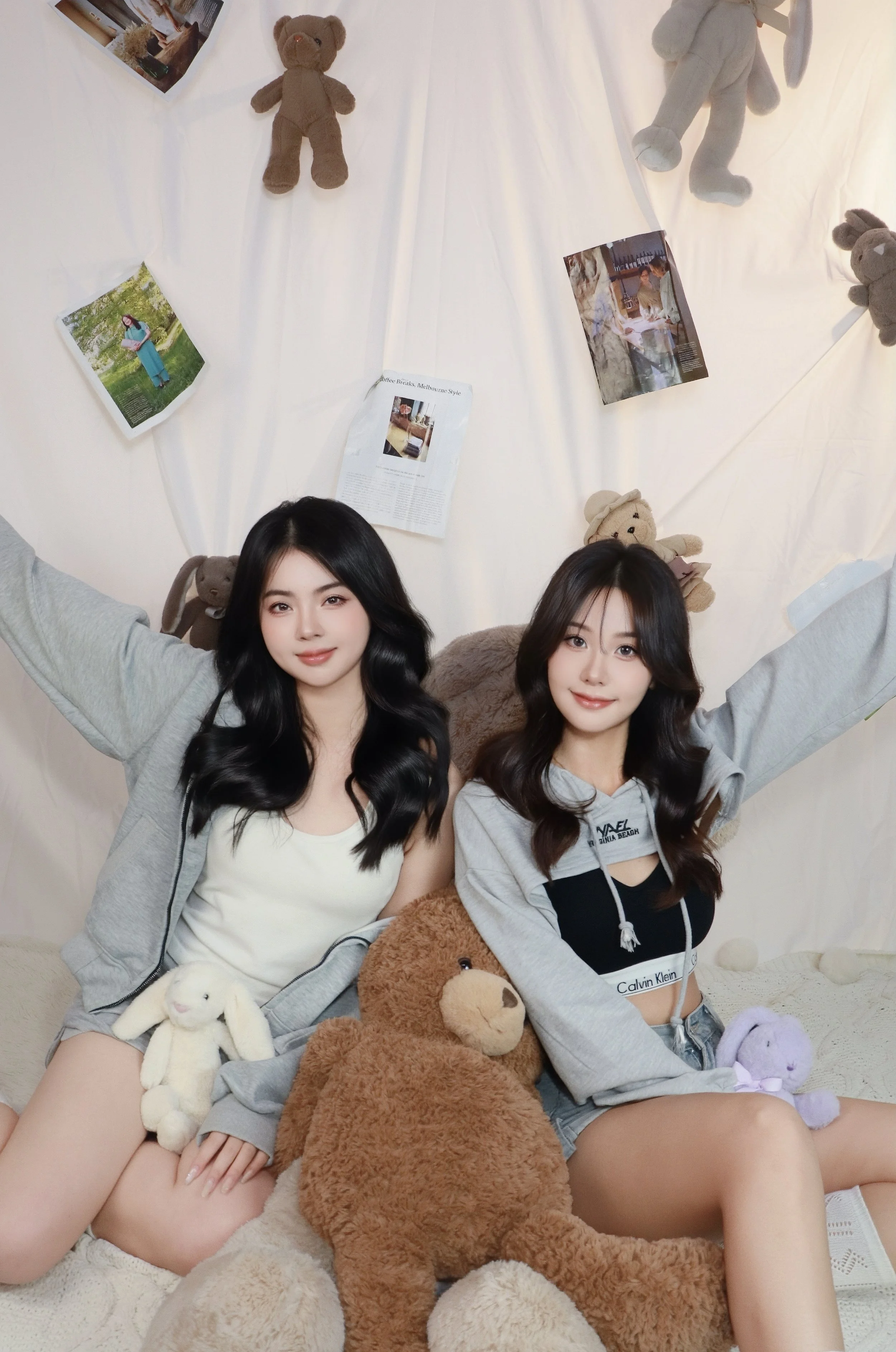 Two friends posing happily in an indoor style photoshoot with a giant brown teddy bear