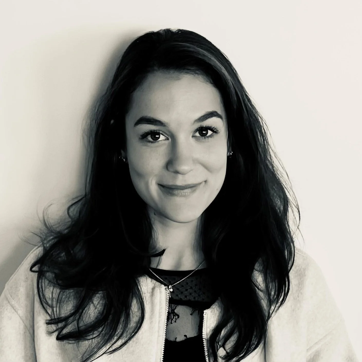 Portrait en noir et blanc d'une femme avec de longs cheveux bouclés, souriant légèrement, portant un sweat léger.