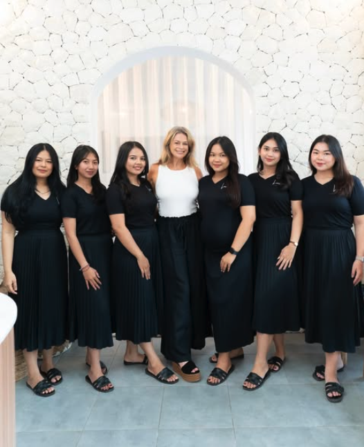 Group of seven women standing together indoors, dressed in black skirts and tops, smiling at the camera.