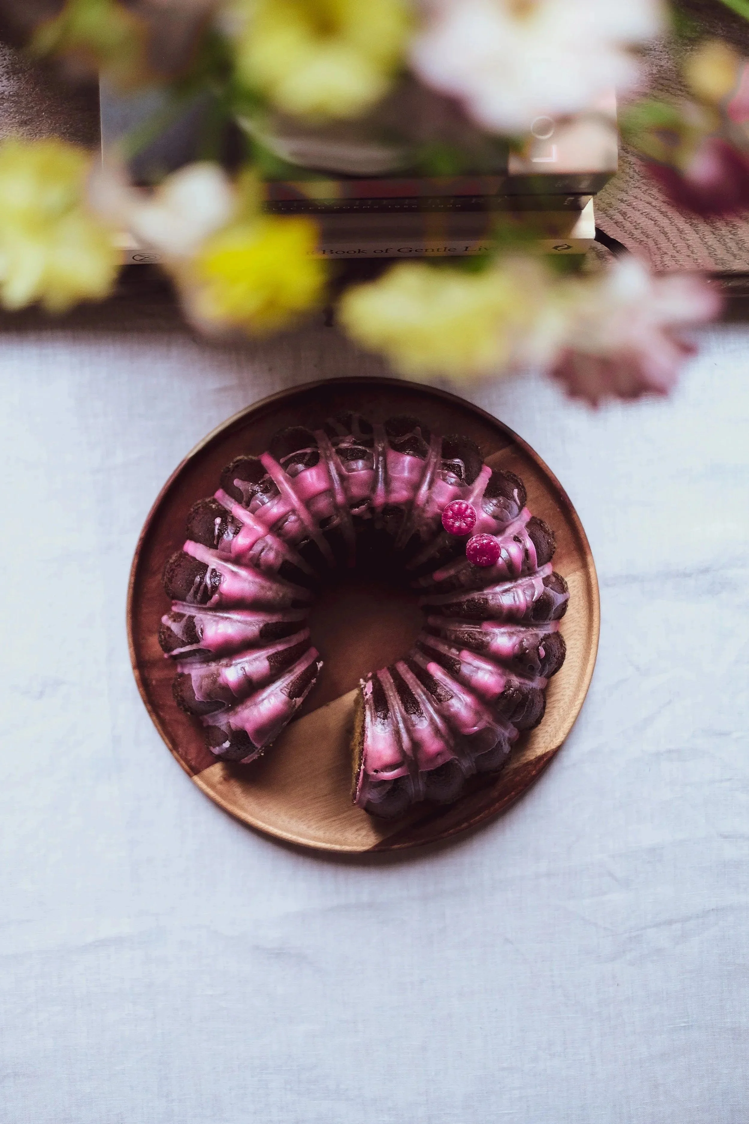 Cream-filled mini donuts with pink icing and raspberry toppings on a wooden plate.