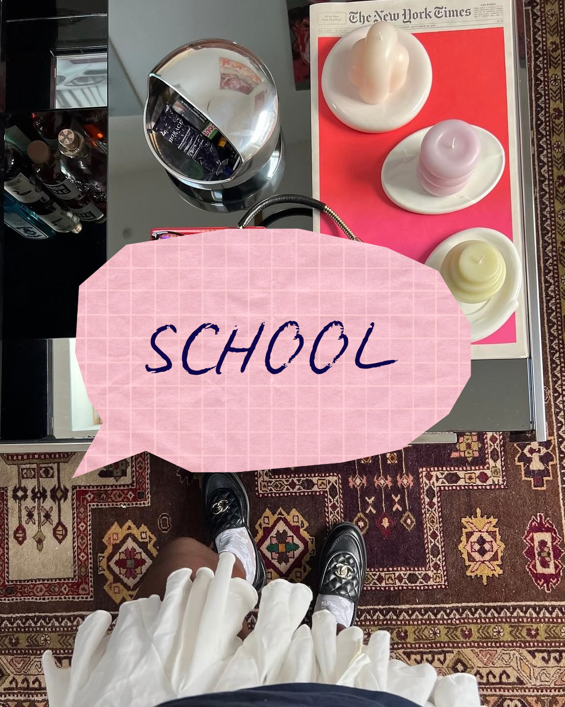 Une table avec trois bougies de cire dans des plats blancs, une bouteille d'eau, un verre rempli d'eau, un journal 'The New York Times', et une personne portant une robe blanche et des chaussures noires à damier. La personne se tient debout sur un ta