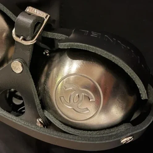 Une paire de lunettes de soleil avec une lentille en métal gravée du logo Chanel, entourée d'une monture noire et de rembourrages en caoutchouc.