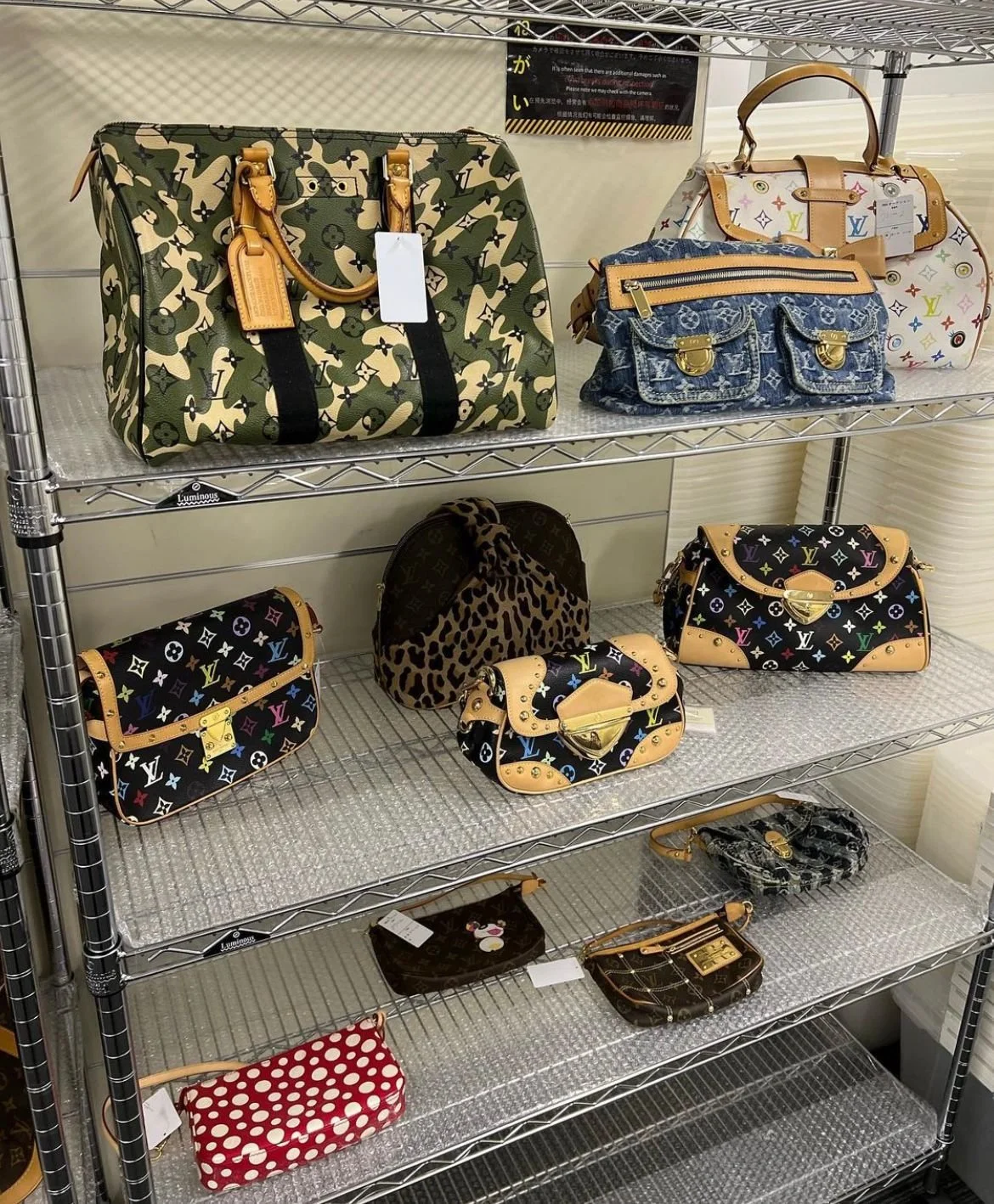 Vitrine avec plusieurs sacs à main de marque Louis Vuitton, dont certains avec des motifs multicolores et d'autres en style classique ou avec imprimés animal, ainsi que des petites pochettes.