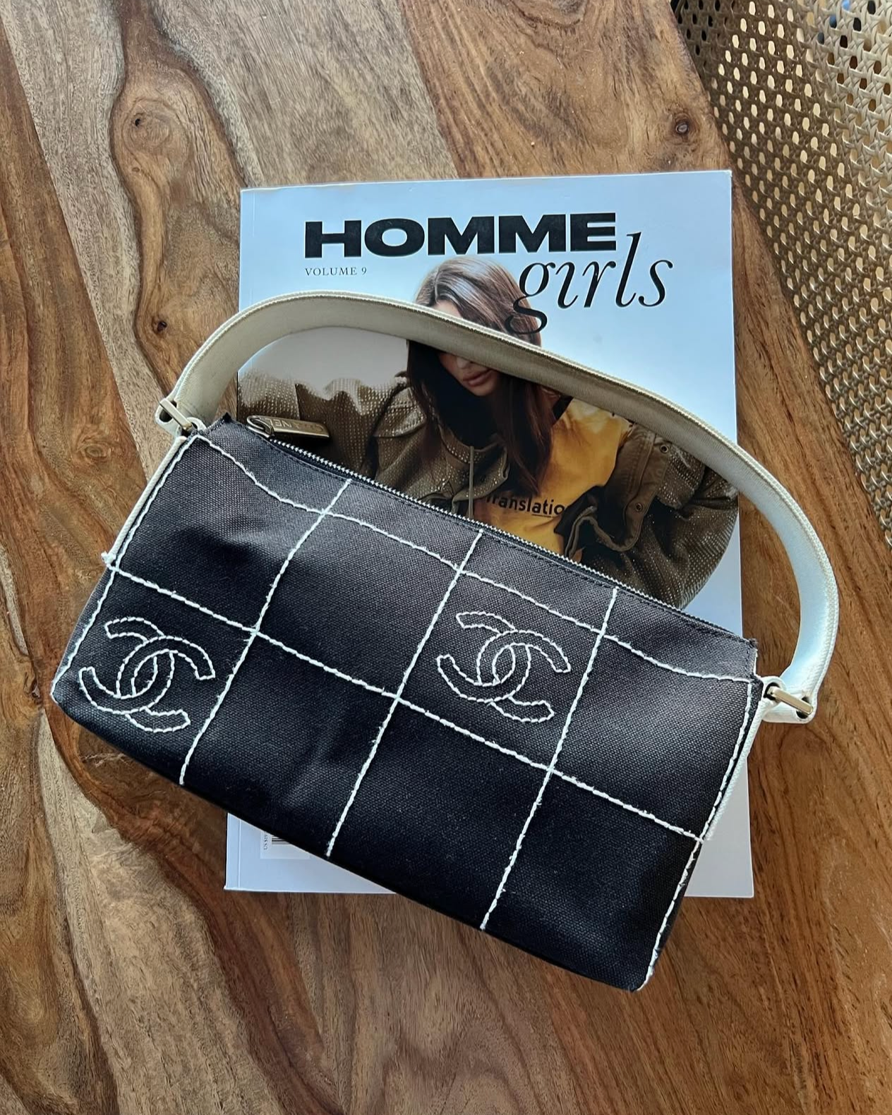 Un sac à main noir avec des lignes blanches et le logo de Chanel, posé sur un magazine intitulé 'Homme, girls'.