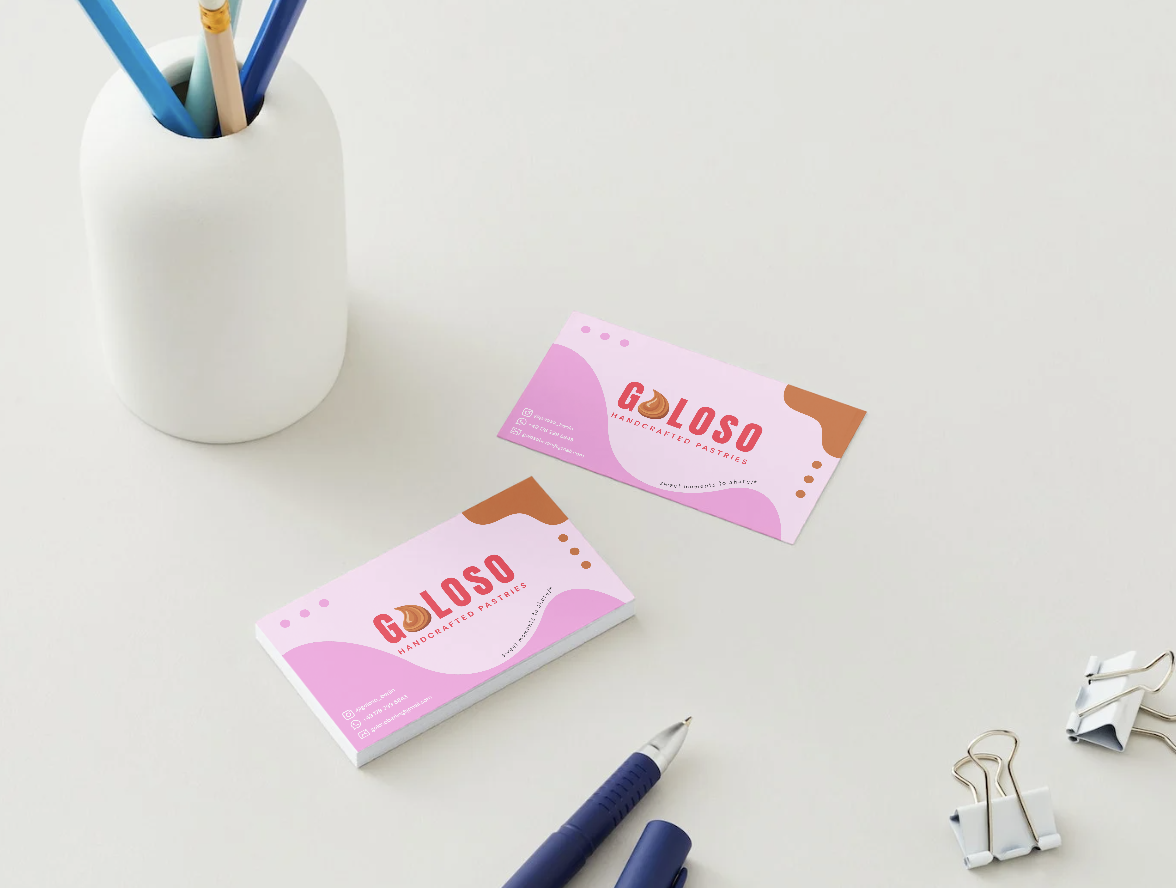 Business cards for Goloso Berlin Brand Handcrafted Pastries on a white desk with office supplies, including a pen, a white container with colored pencils, and binder clips.