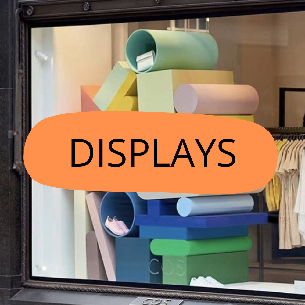 Colorful abstract sculpture made of various geometric shapes, displayed behind a glass window with the word 'DISPLAYS' overlaid in bold letters.