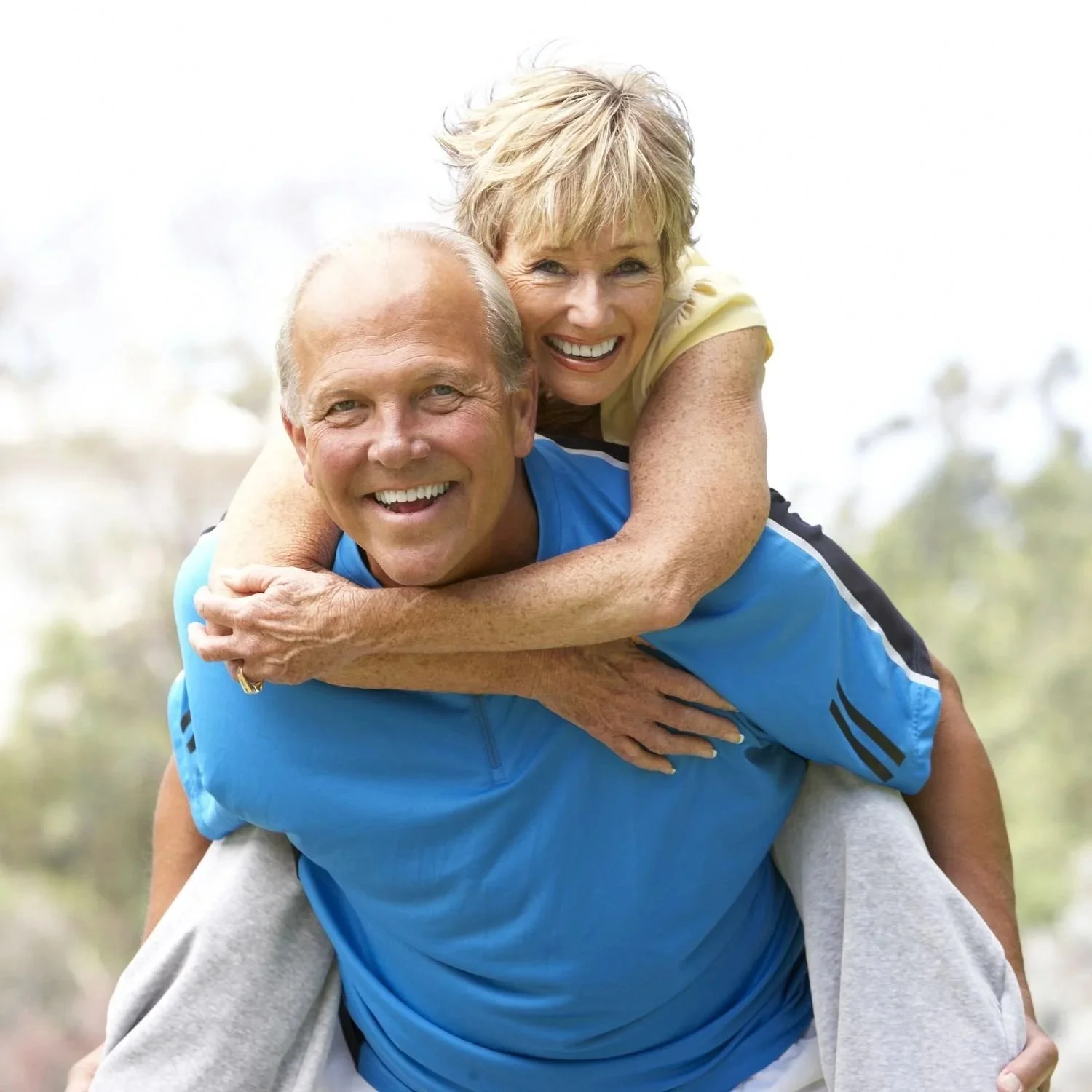 A happy elderly couple enjoying an outdoor activity, with the woman giving the man a piggyback ride.