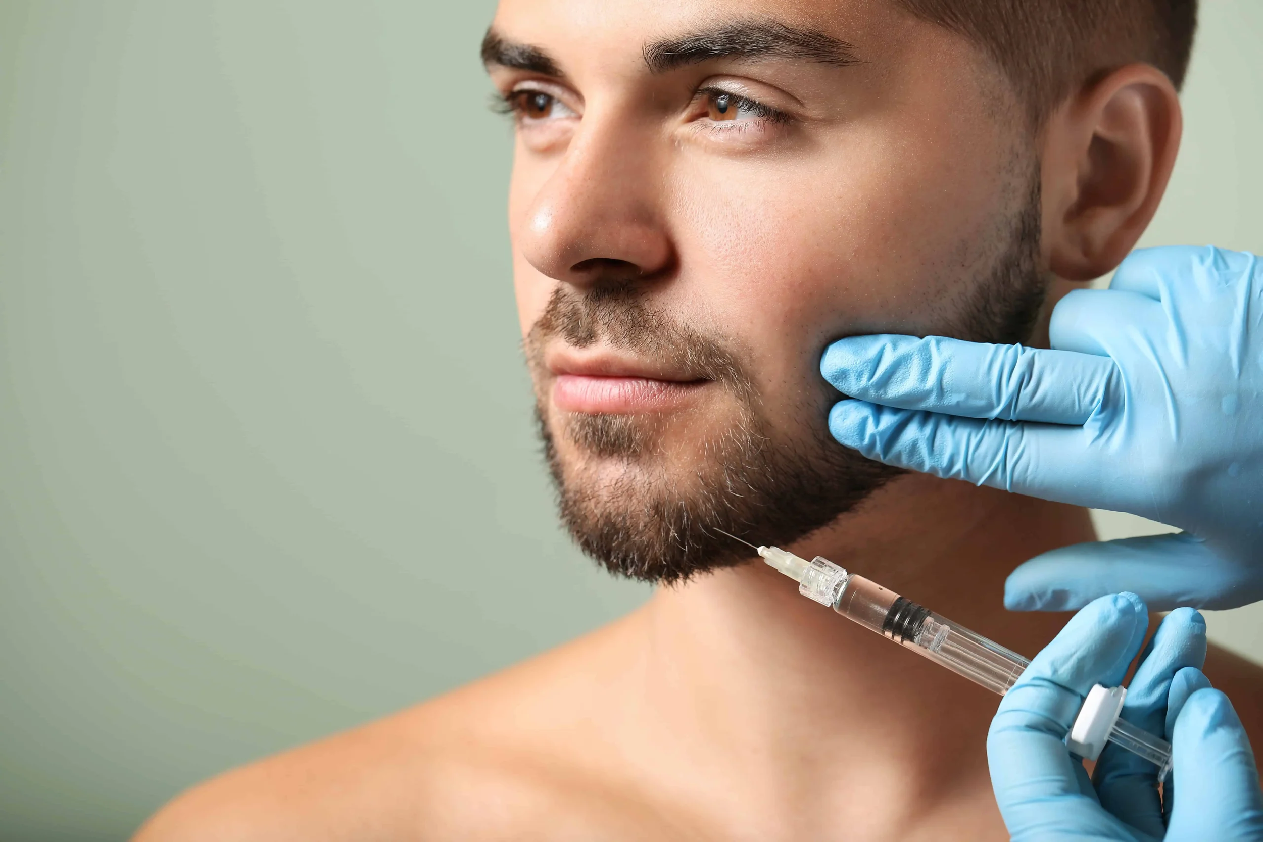 Male model receiving precise chin filler injection administered by a professional with gloved hands.