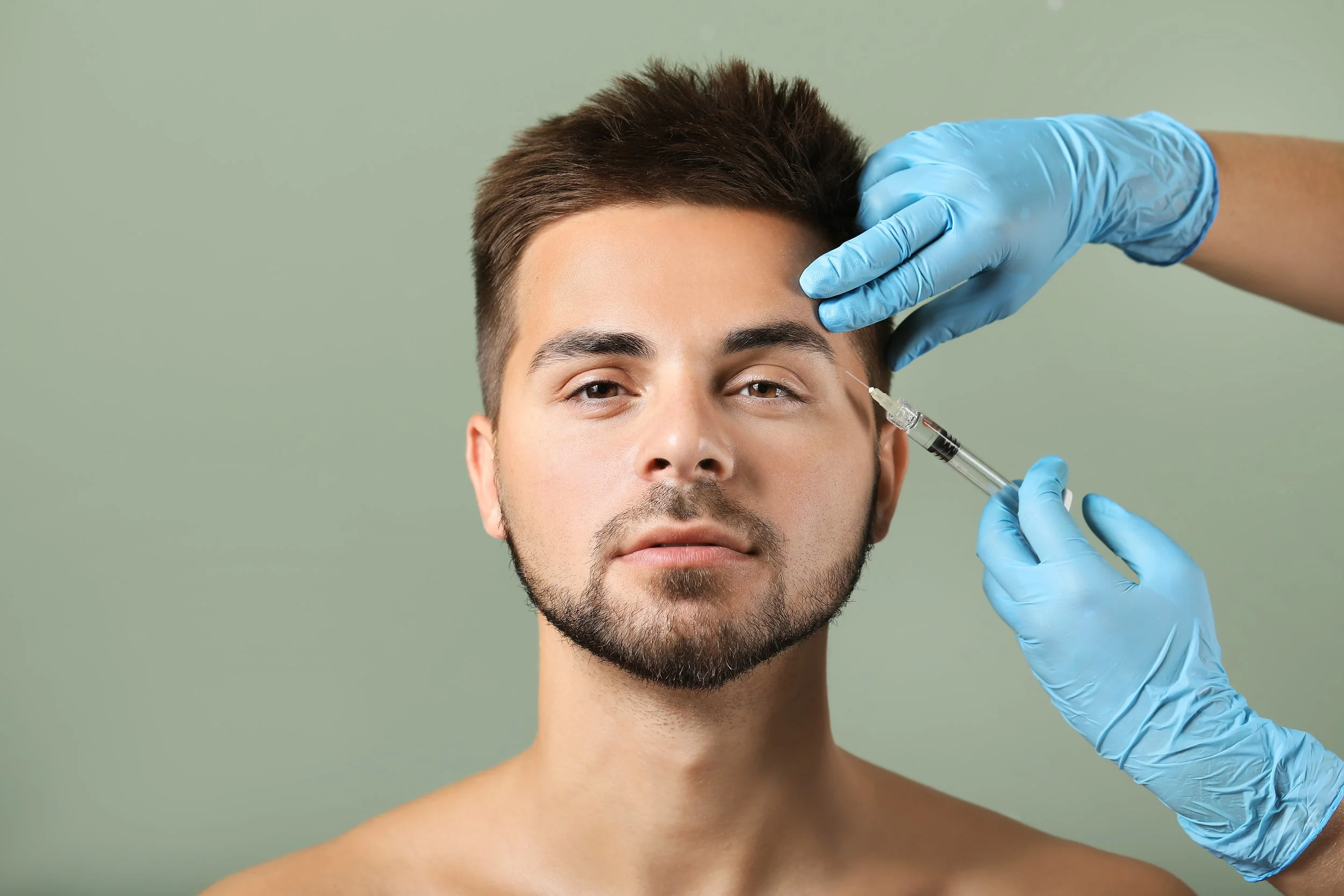 Male model receiving precise temple filler injection administered by a professional with gloved hands.