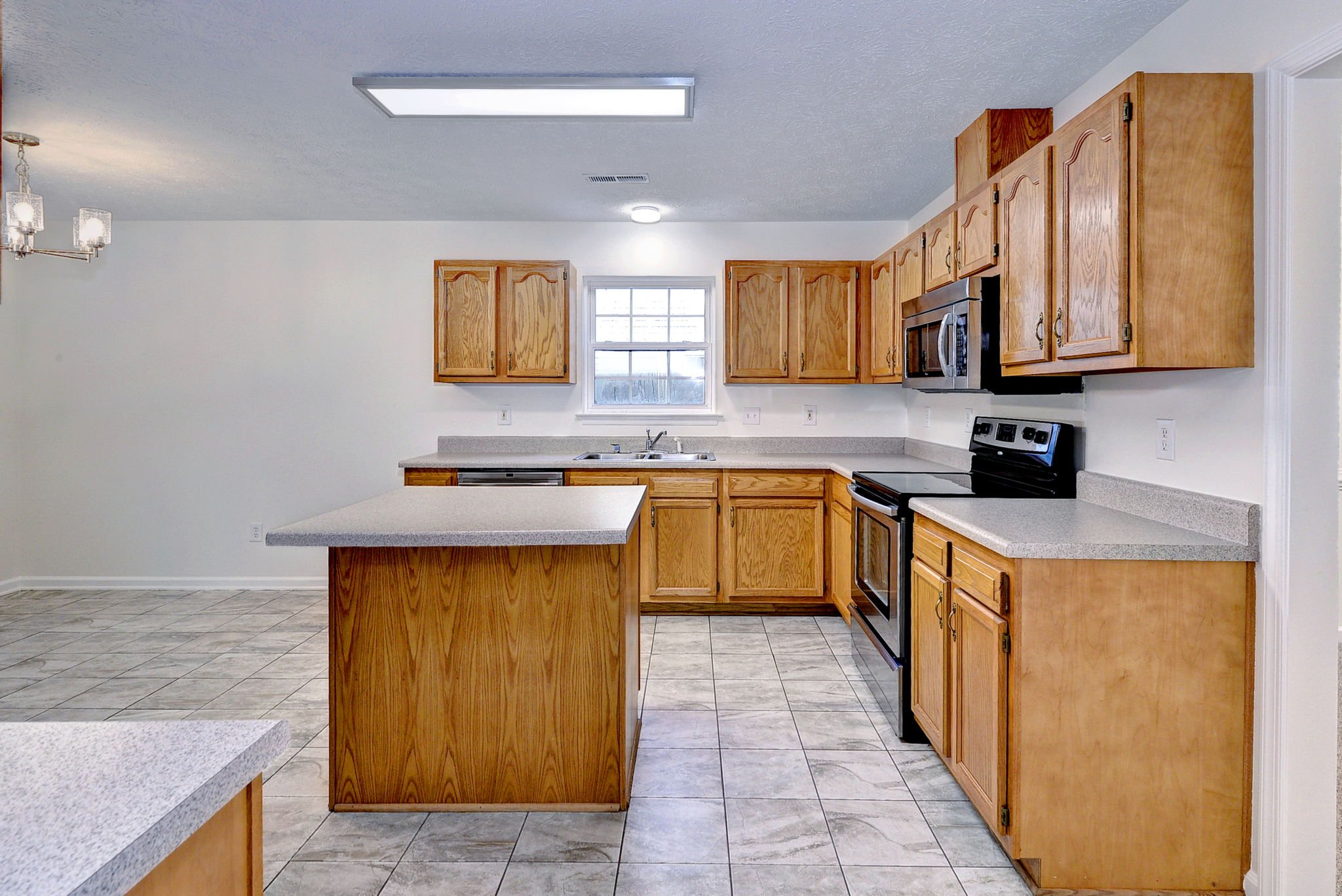 A kitchen with wooden cabinets, a window, a black stove, a microwave, and a central island with a countertop.