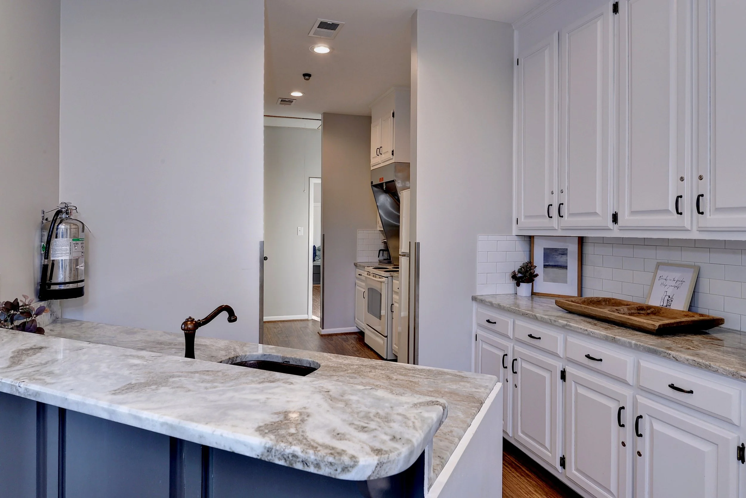 Kitchen with white cabinets, marble countertops, and a small island with a sink.