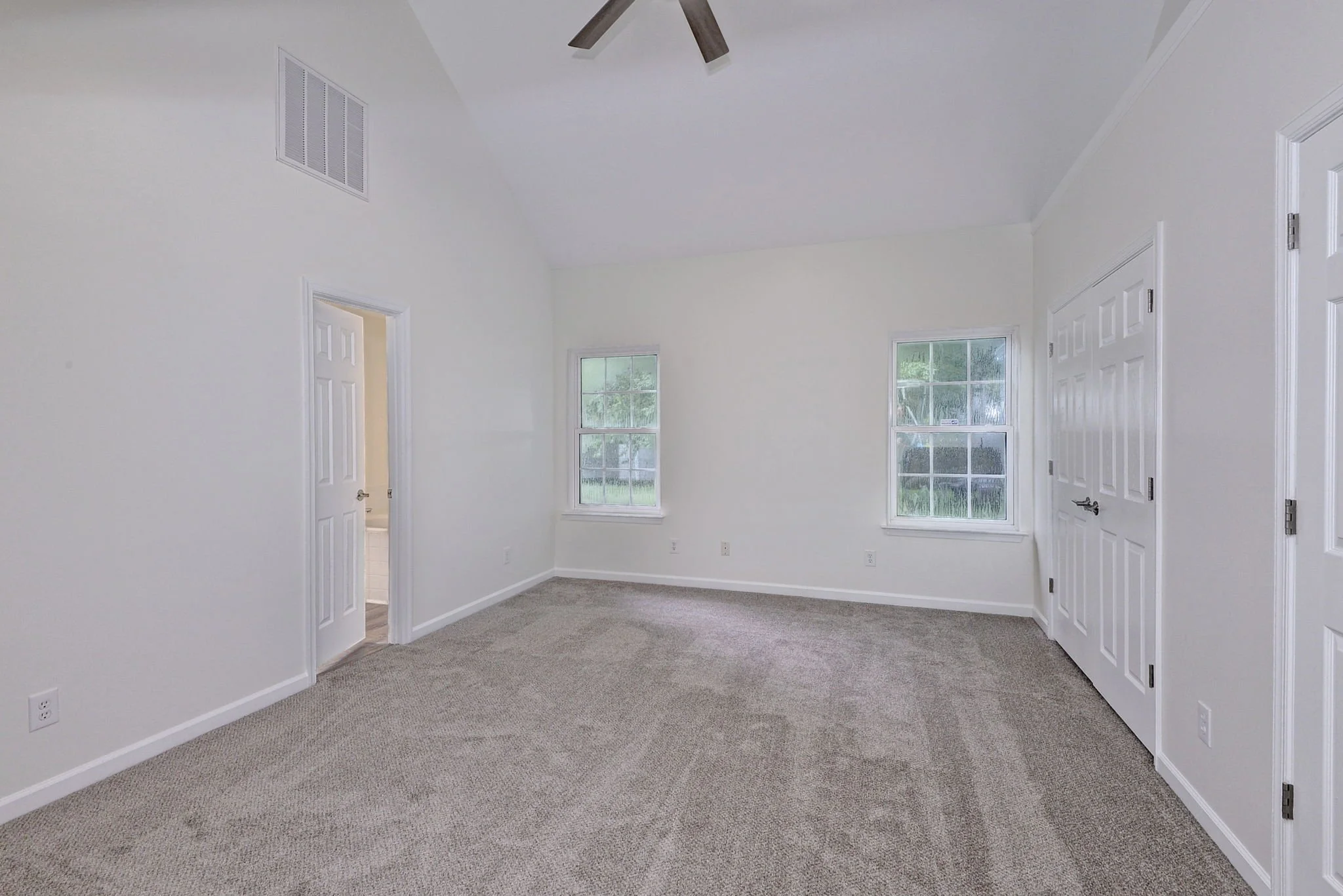 Empty room with beige carpet, white walls, two windows, and white doors.