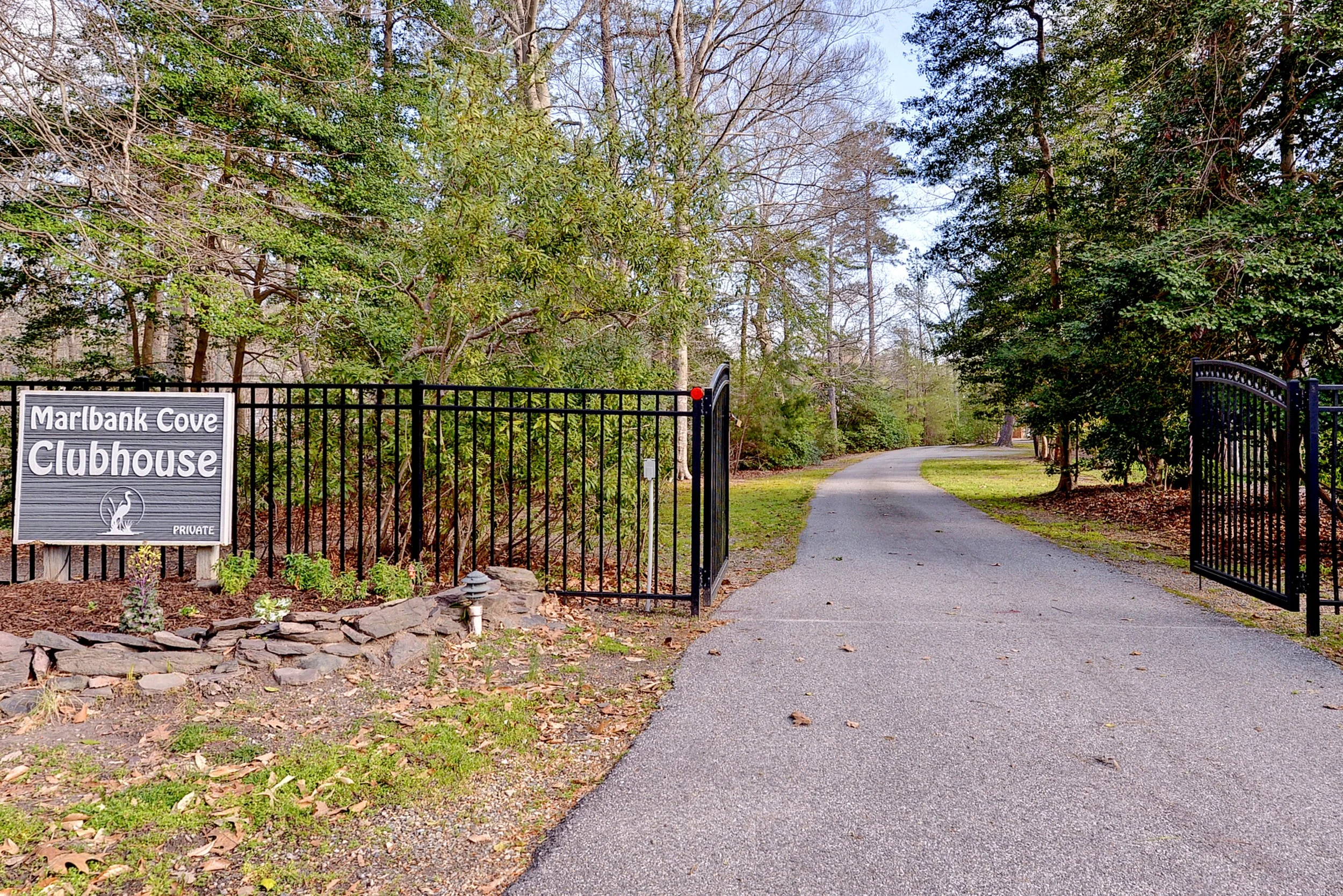 Entrance gate to Maribank Cove Clubhouse with a sign and a paved path leading into a wooded area.
