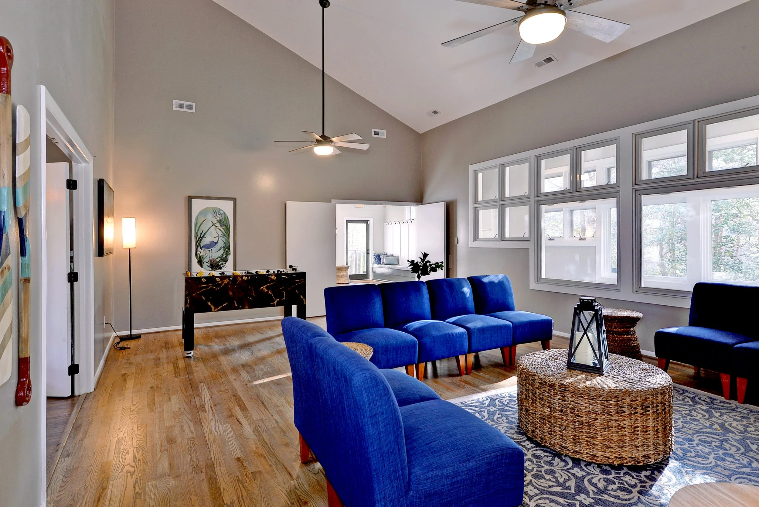 Living room with blue couches, large windows, artwork, and hardwood floors.