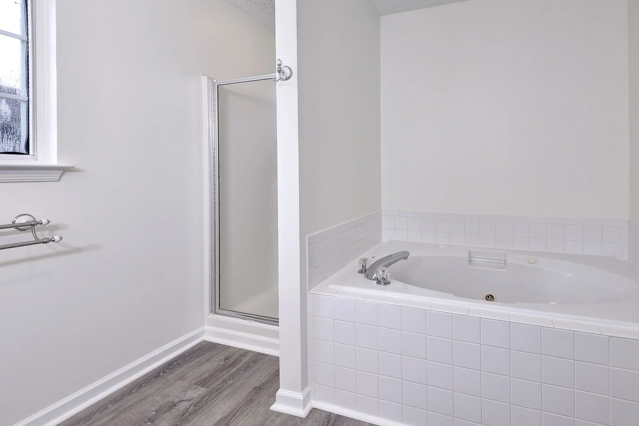 Bathroom with white walls, a bathtub with a tiled surround, a window with frosted glass, and a shower stall with a glass door.