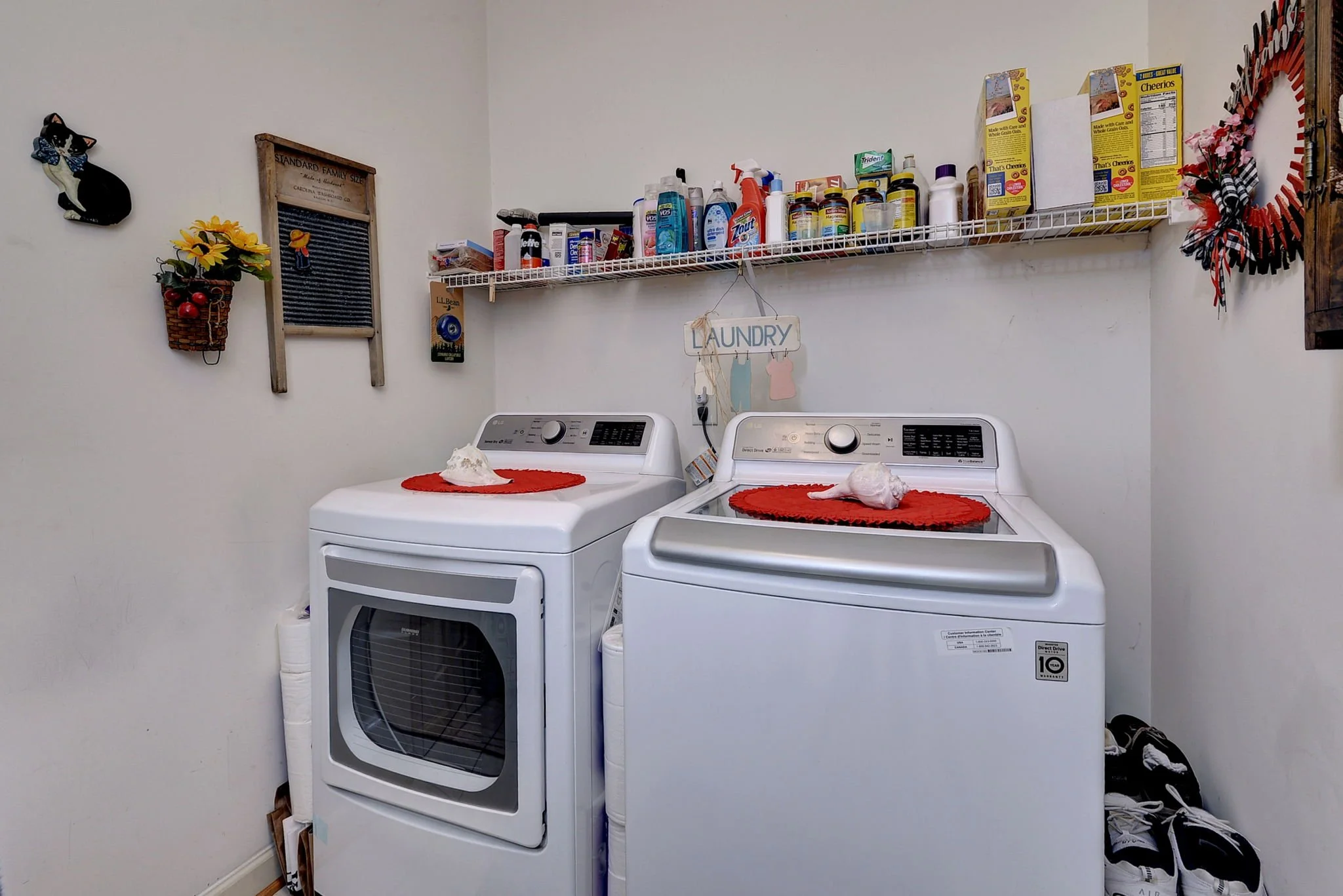 A laundry room with a washer and dryer, a shelf with cleaning supplies above them, and decorative items on the wall.