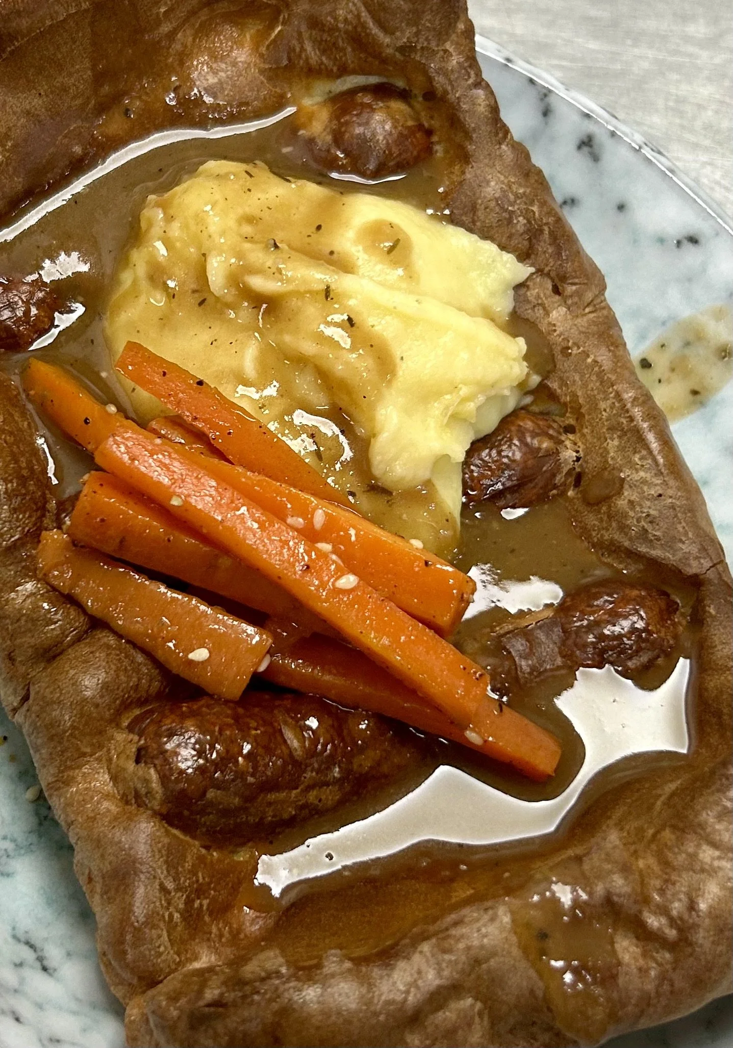 Toad in the Hole: Yorkshire pudding with sausages, mashed potatoes, and gravy, garnished with carrot sticks.