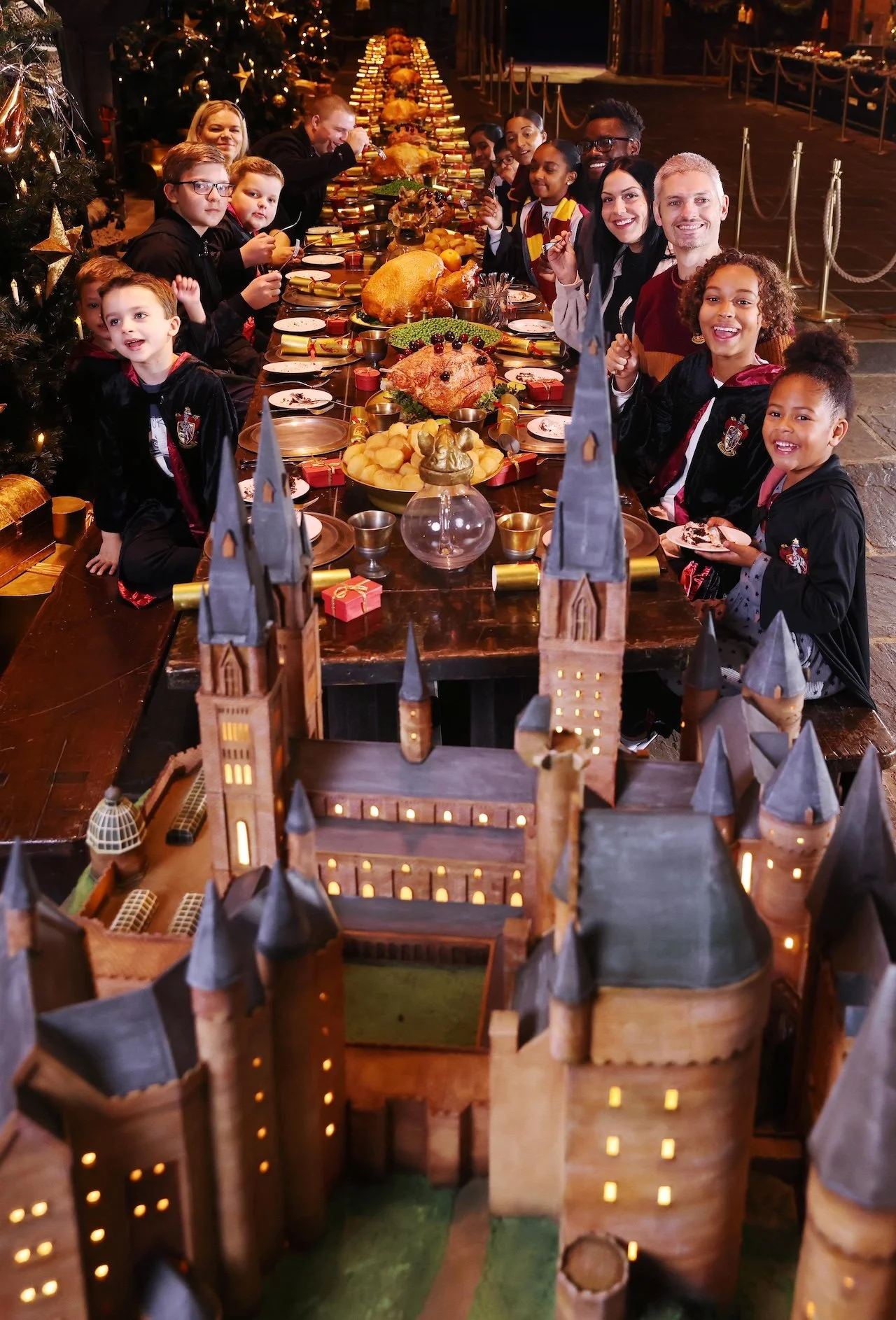 A group of excited children enjoying lunch in the Great Hall at the Warner Bros. Studio Tour London – The Making of Harry Potter, eagerly anticipating a taste of the massive Hogwarts Castle cake.