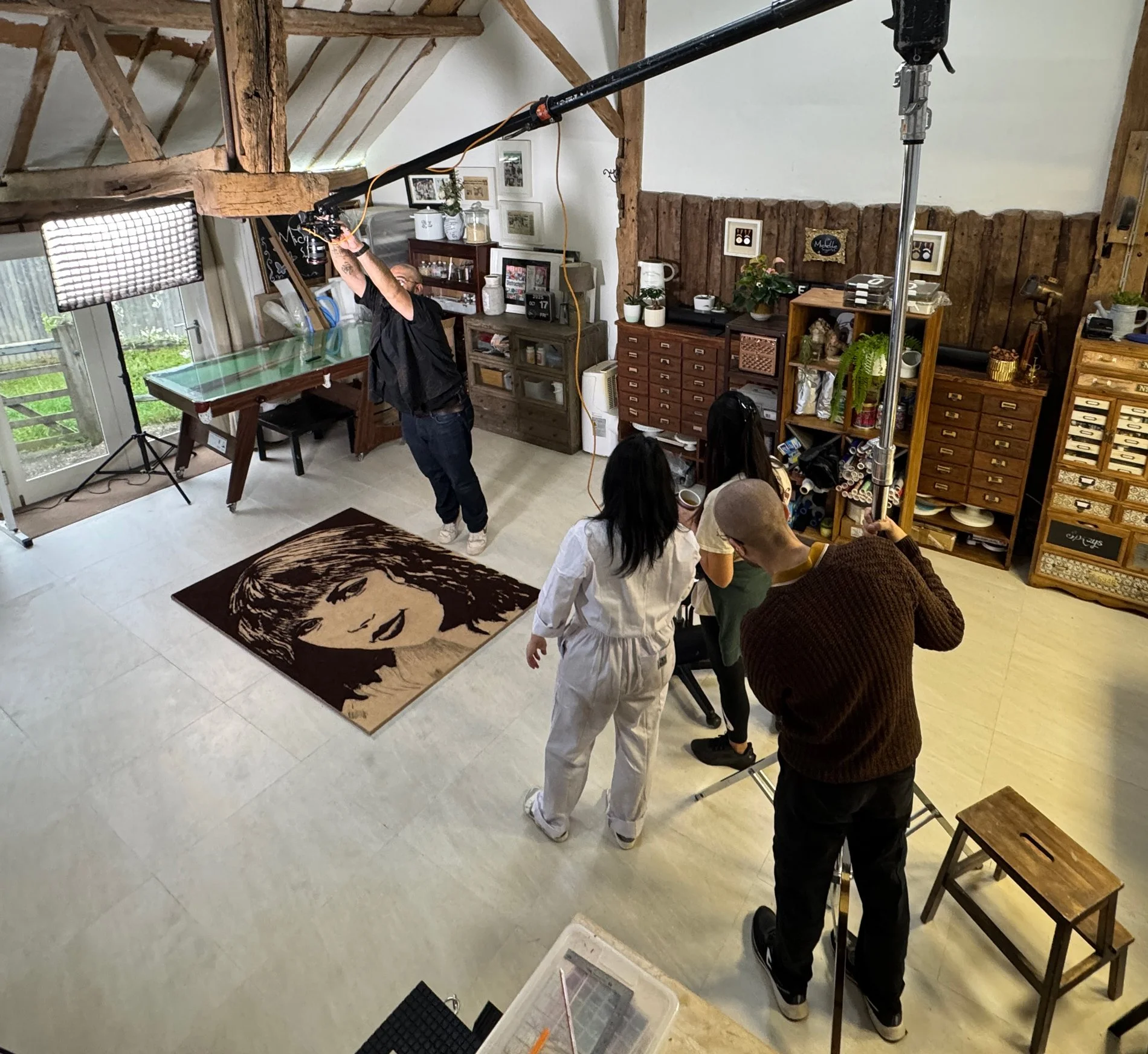 Behind-the-scenes shot of cake artist Michelle Wibowo collaborating with a BBC cameraman and film crew while creating a Taylor Swift portrait out of coffee grounds for the TV show Go Get Arty.