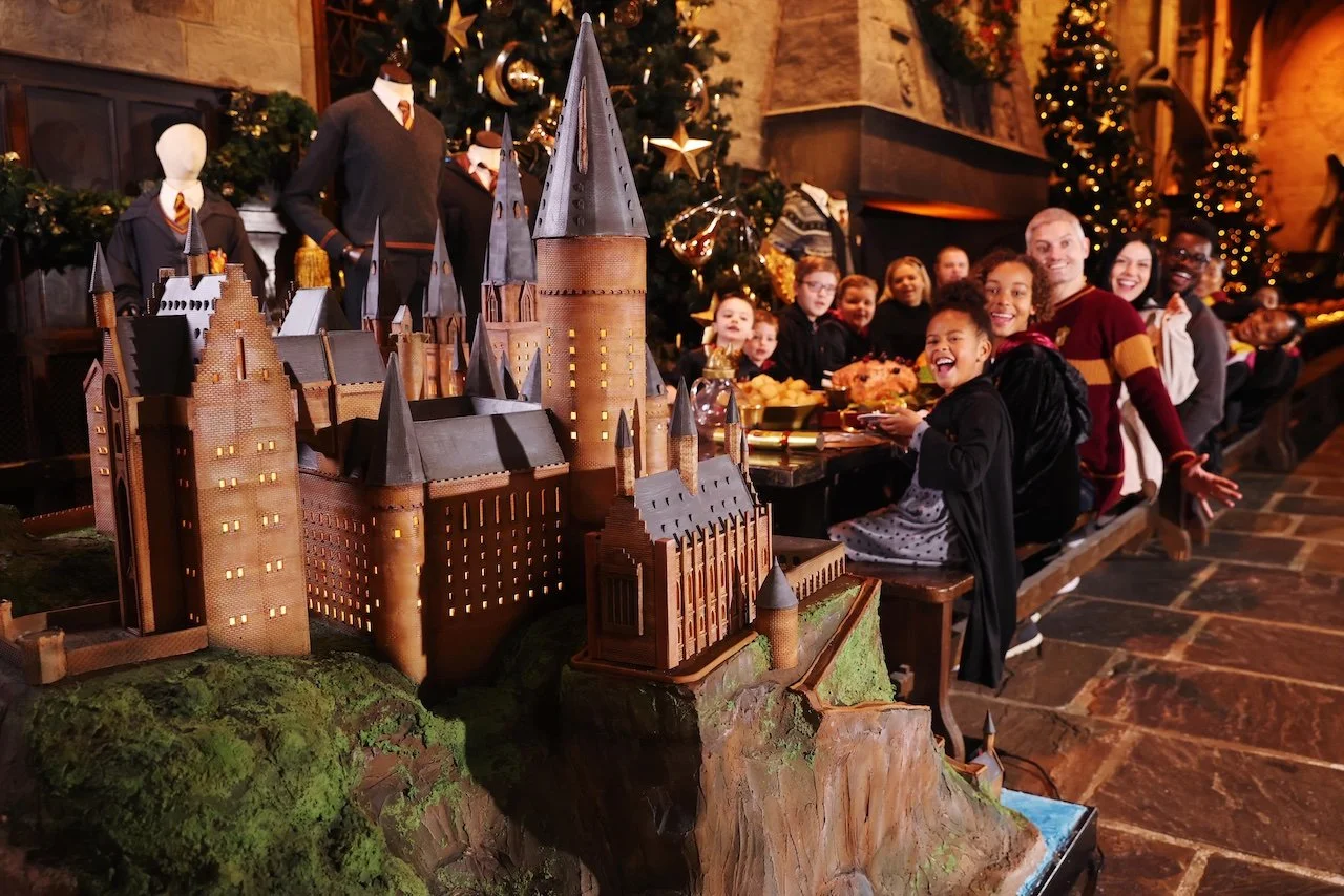 A group of Harry Potter fans enjoying a meal in the Great Hall at the Warner Bros. Studio Tour London – The Making of Harry Potter, with a stunning replica of Hogwarts Castle in the foreground.