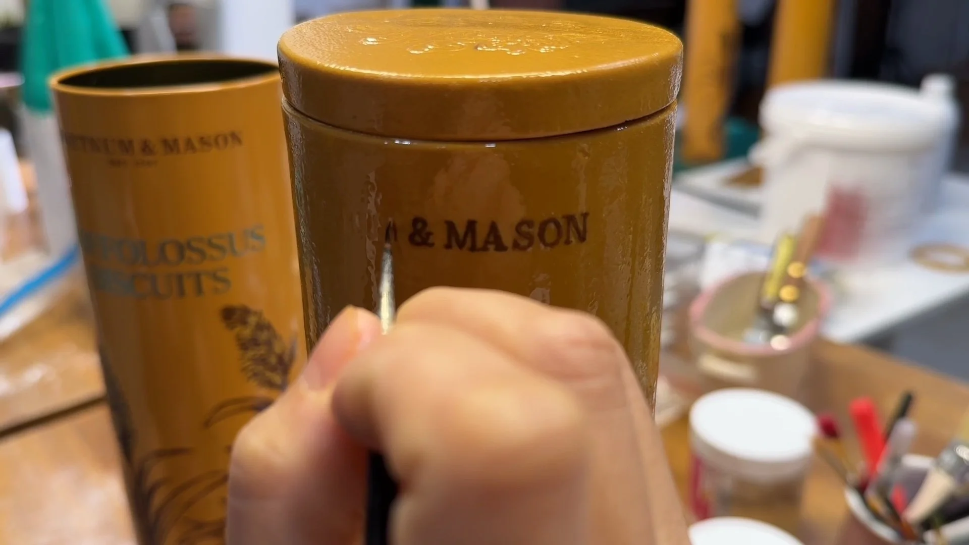Food Artist Michelle Wibowo is applying hand-painted details on the biscuit tin.