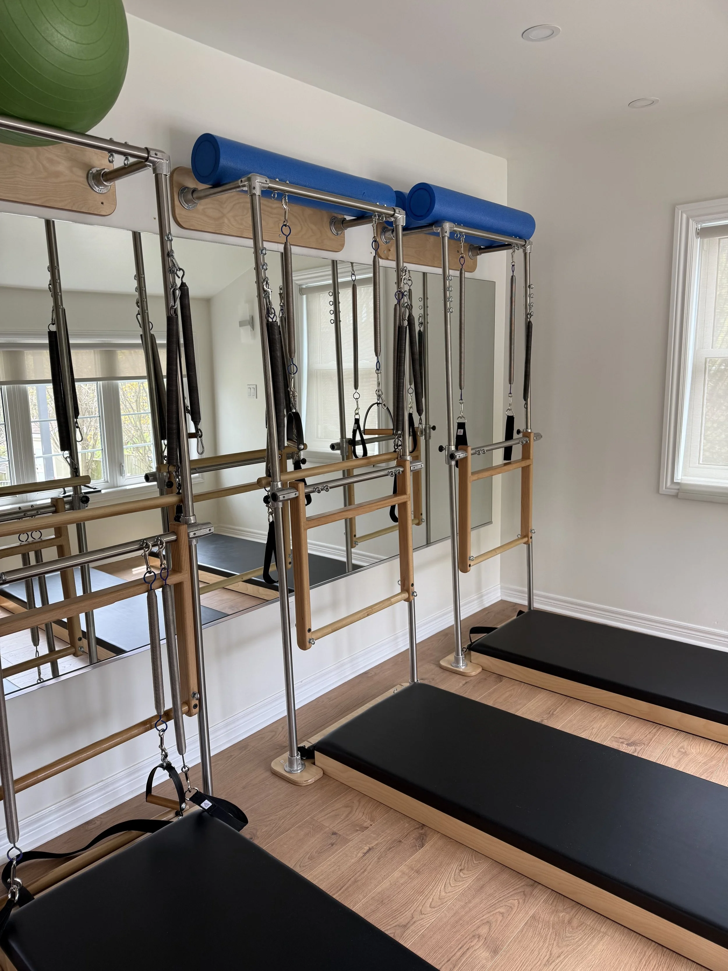 Pilates reformer equipment with black mats and large exercise balls in a bright studio.